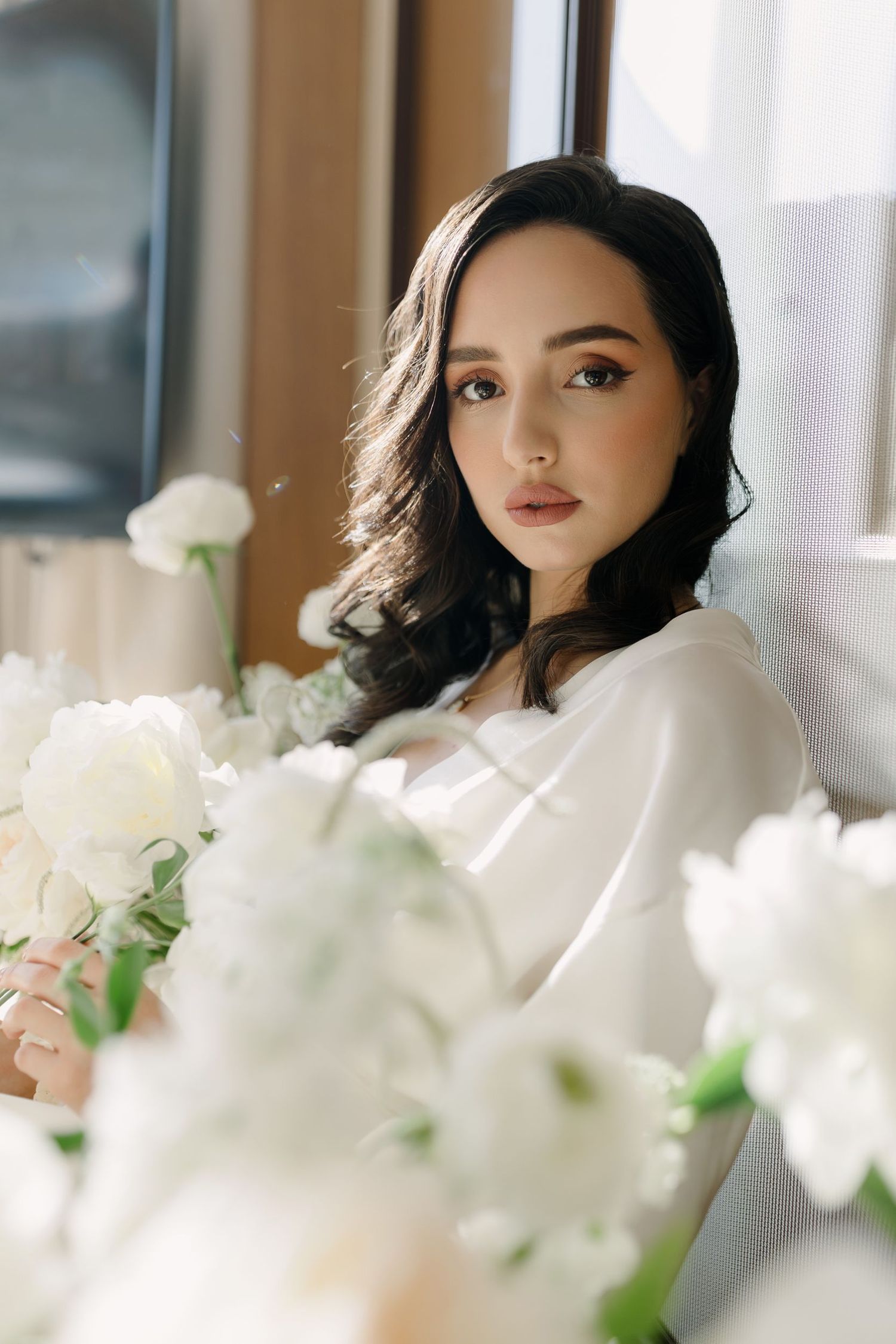 Elegant portrait surrounded by white flowers near window with natural lighting.