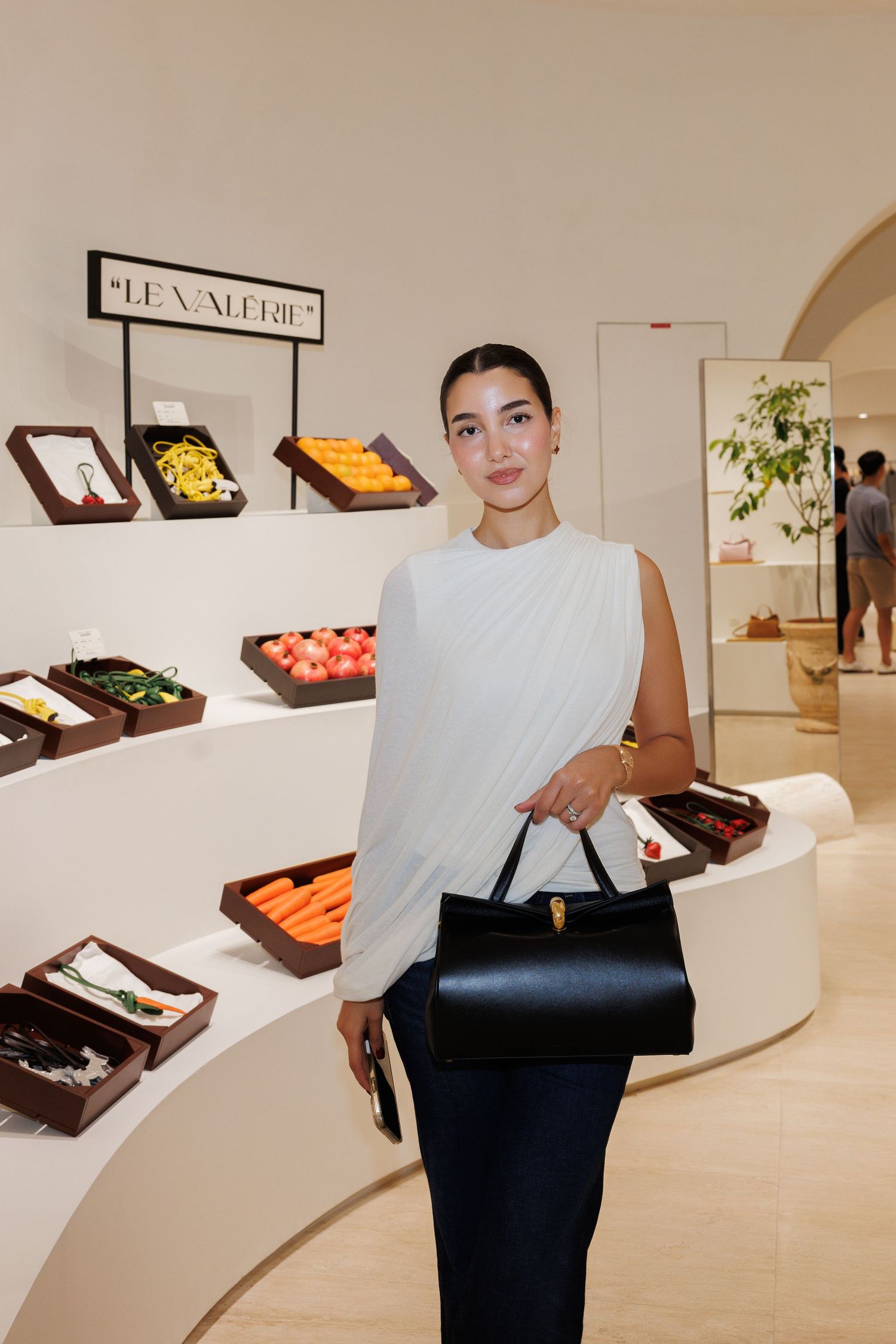 Person in white top displaying handbags in a modern gallery with wooden display cases.