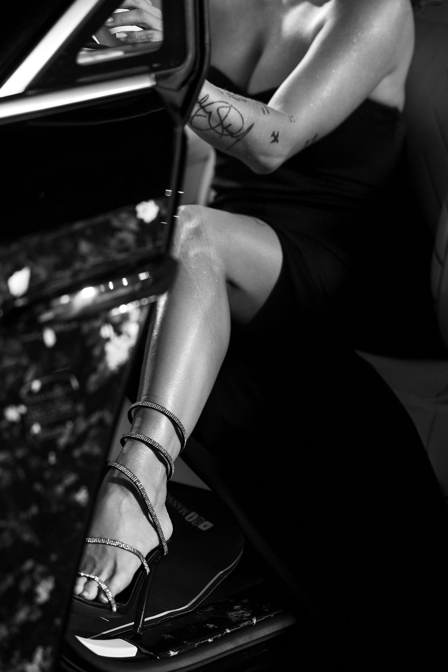 Black and white image of high heels and legs in a luxury car interior.