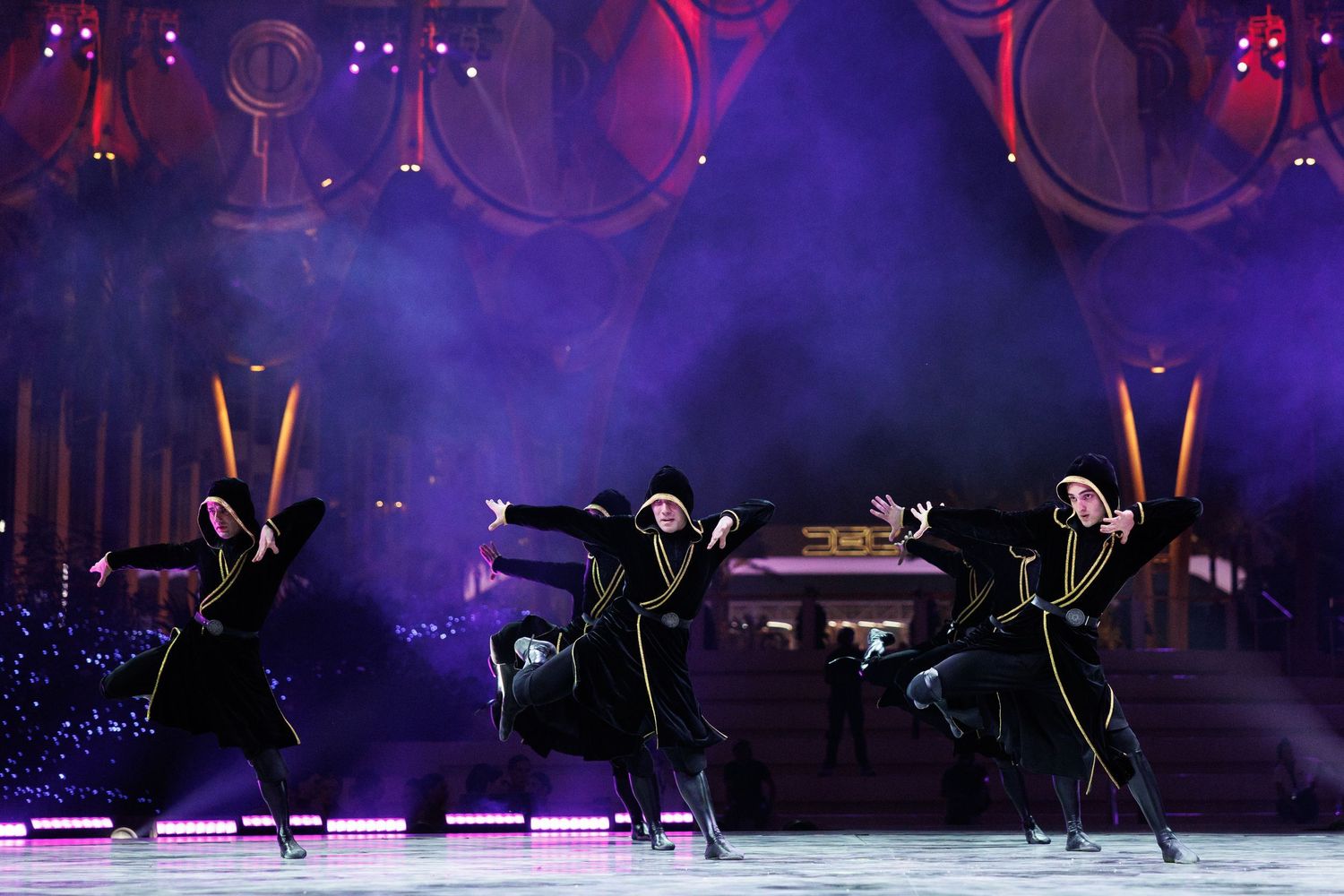 Silhouetted performers dance on stage with purple lighting effects.