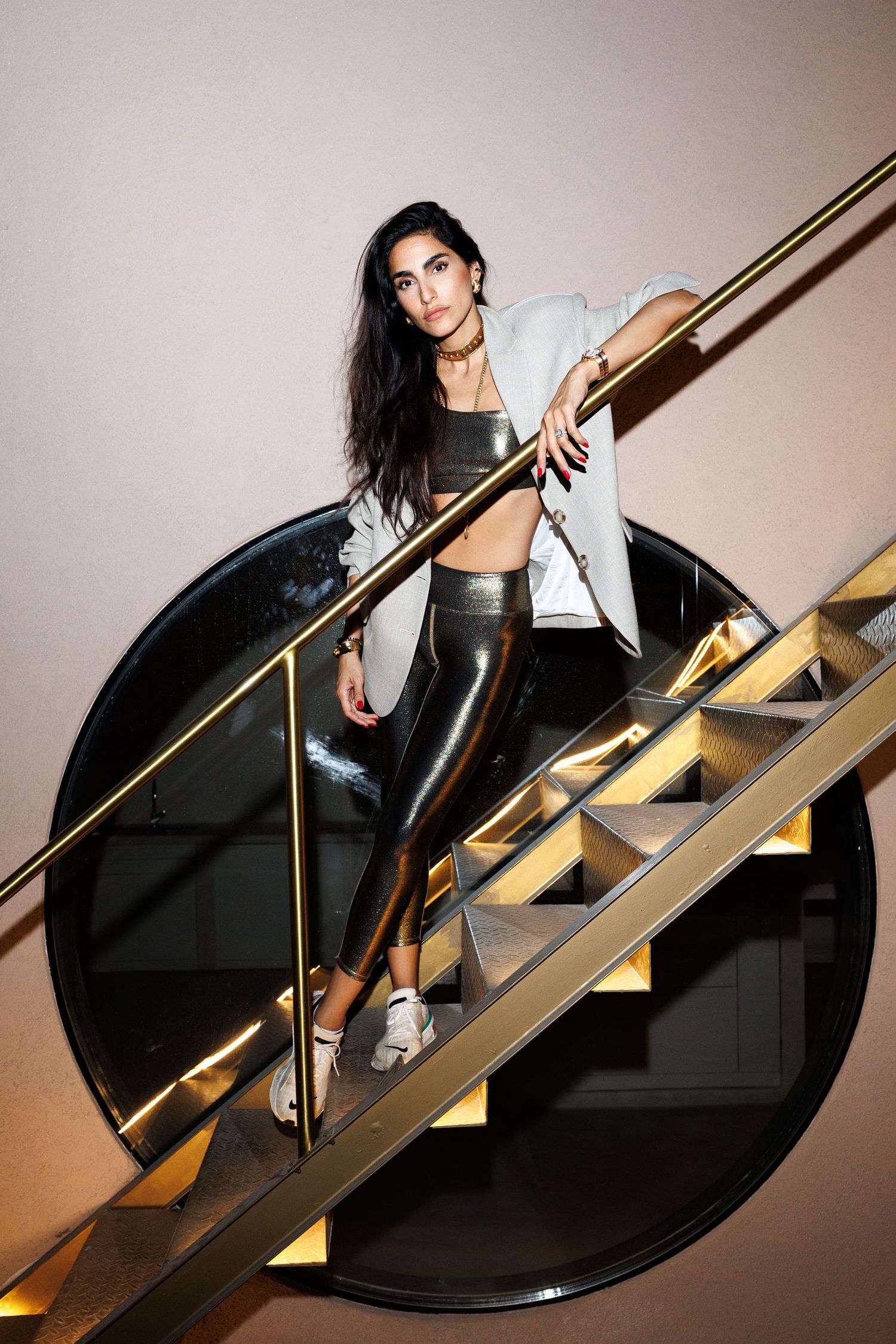 Person in black outfit ascending modern staircase with gold railing in dramatic lighting.