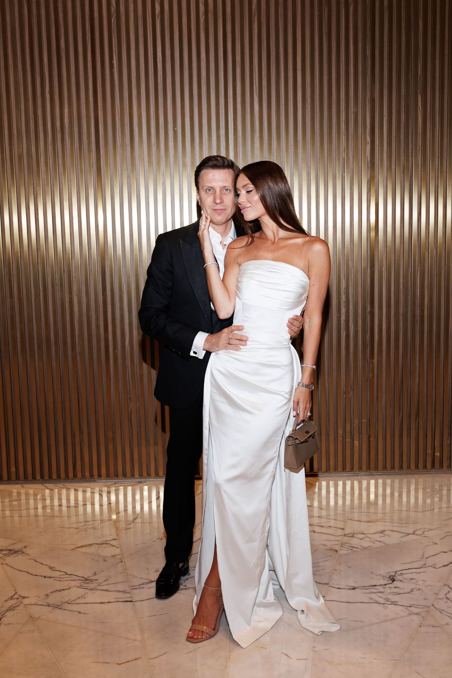 Formal couple poses against metallic backdrop at elegant evening event.