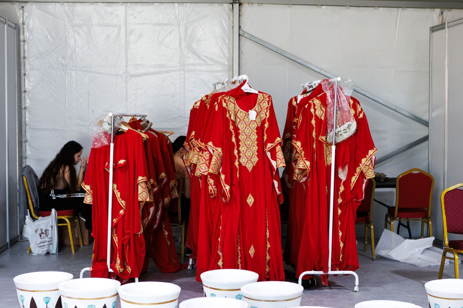 Traditional red and gold embroidered garments hanging on clothing racks in a backstage area.