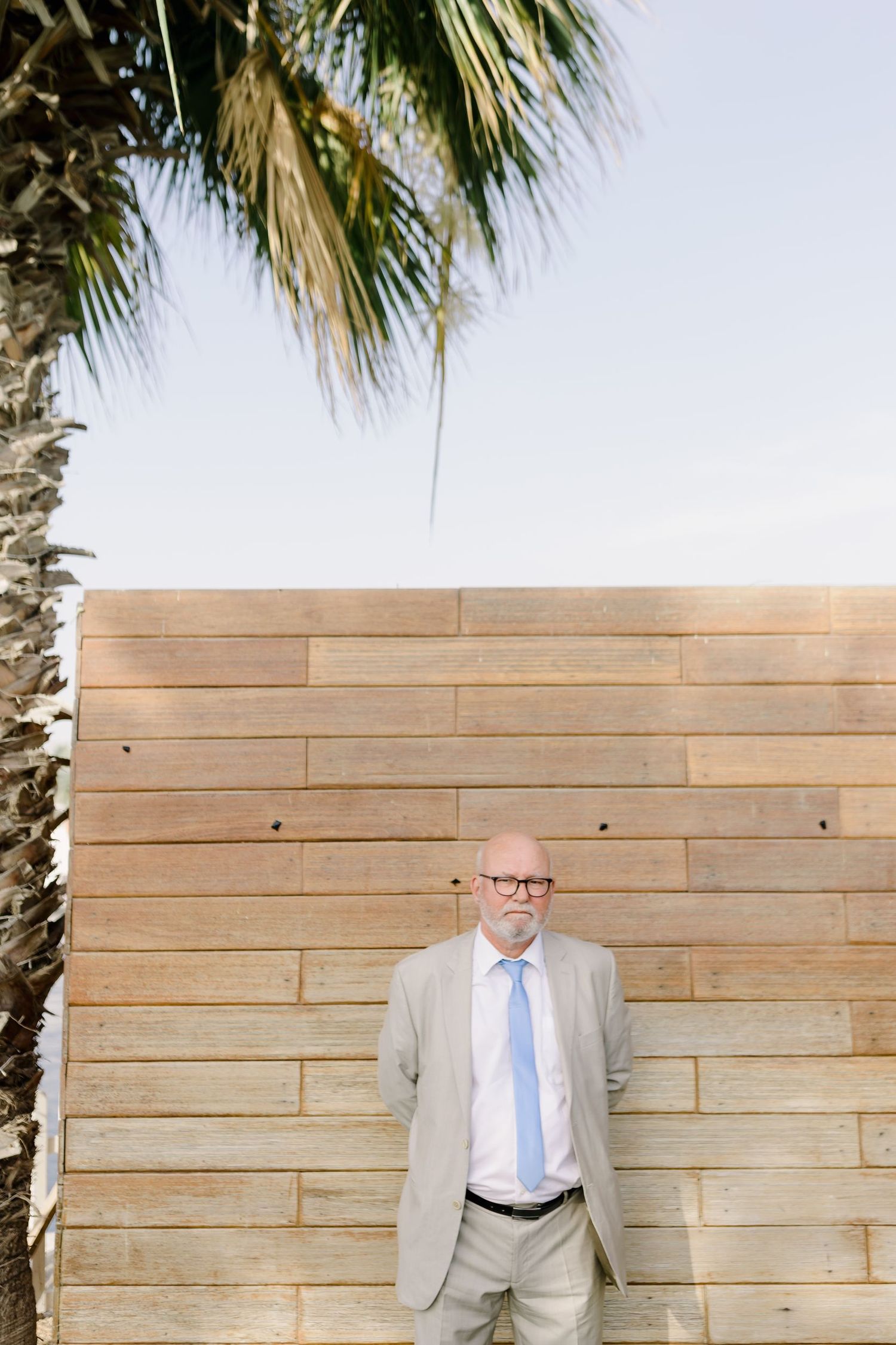 Formal portrait against a wooden plank wall with palm trees overhead.