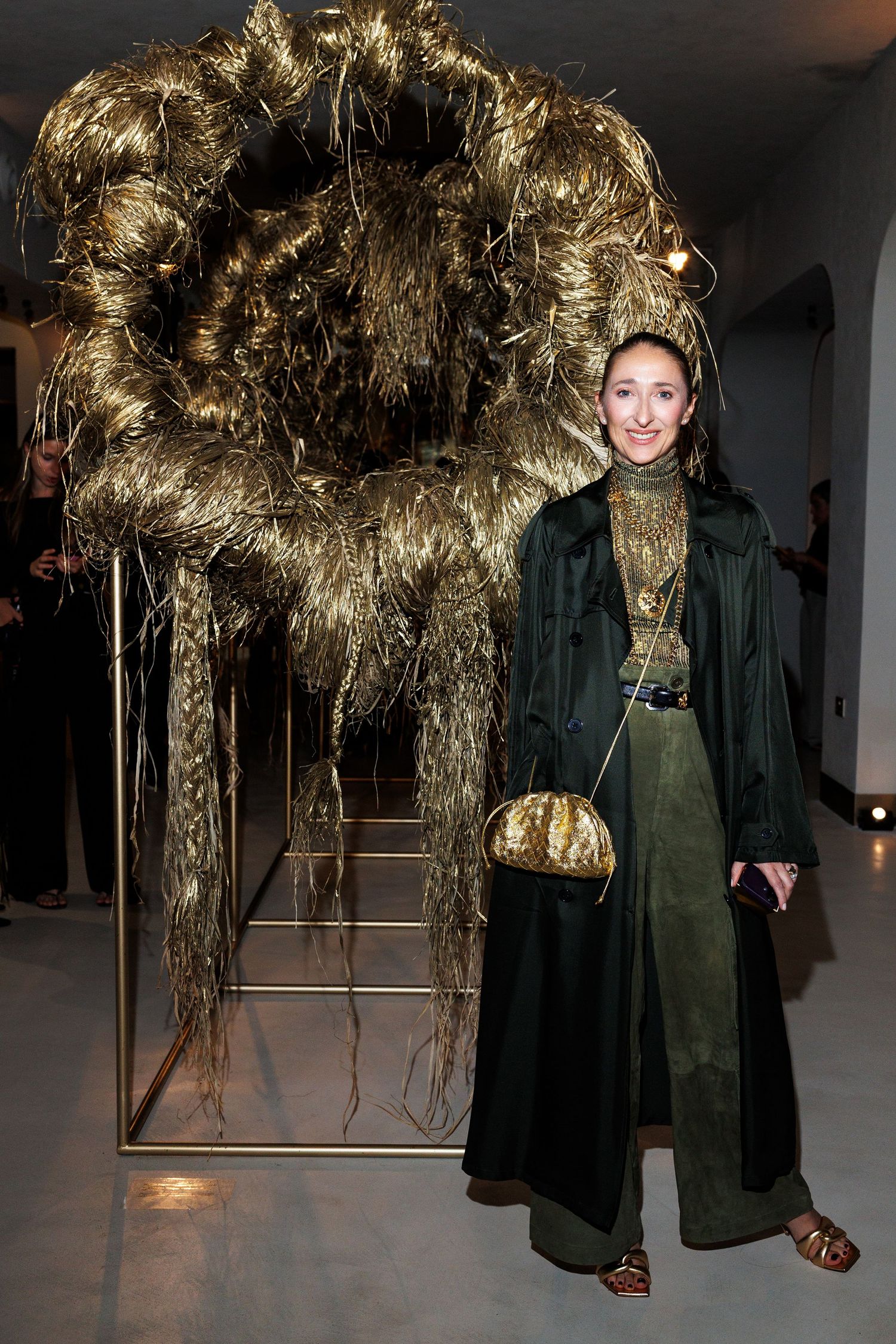 Two figures stand beneath a large golden metallic art installation in a gallery space.