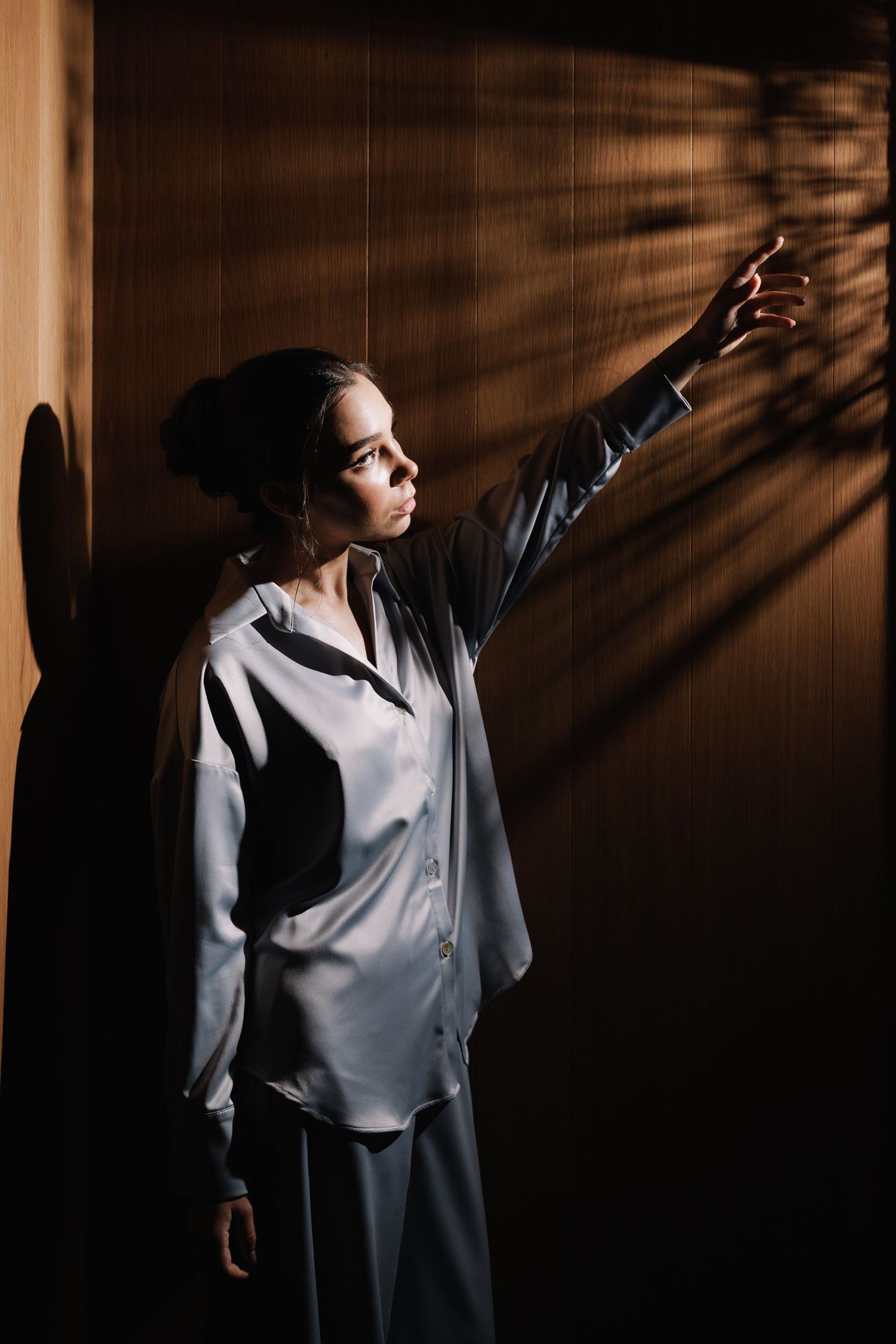 Figure in silk pajamas reaching up dramatically in shadowy lighting.