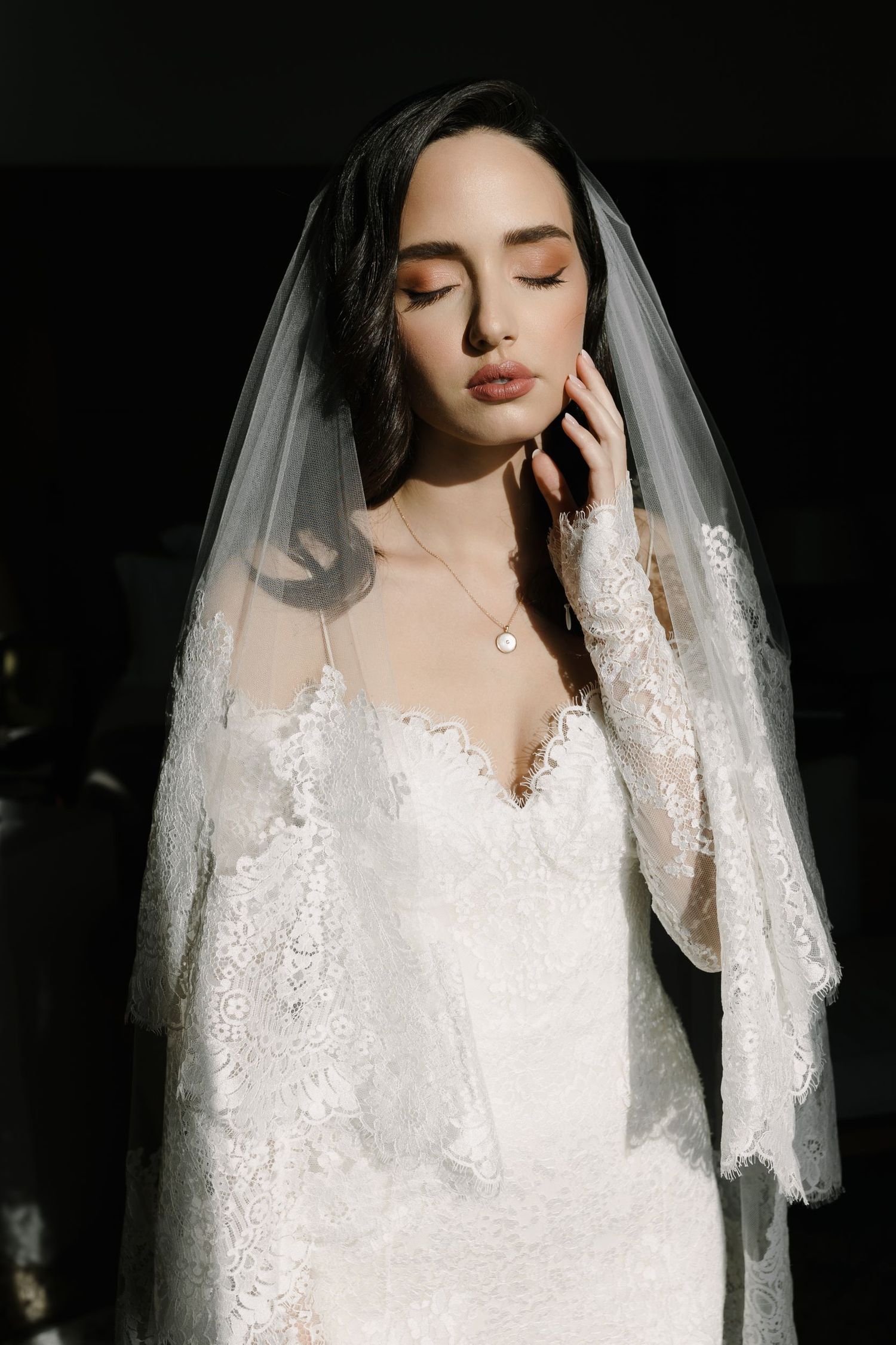 Ethereal bridal portrait featuring intricate lace details and a flowing veil against dark backdrop.