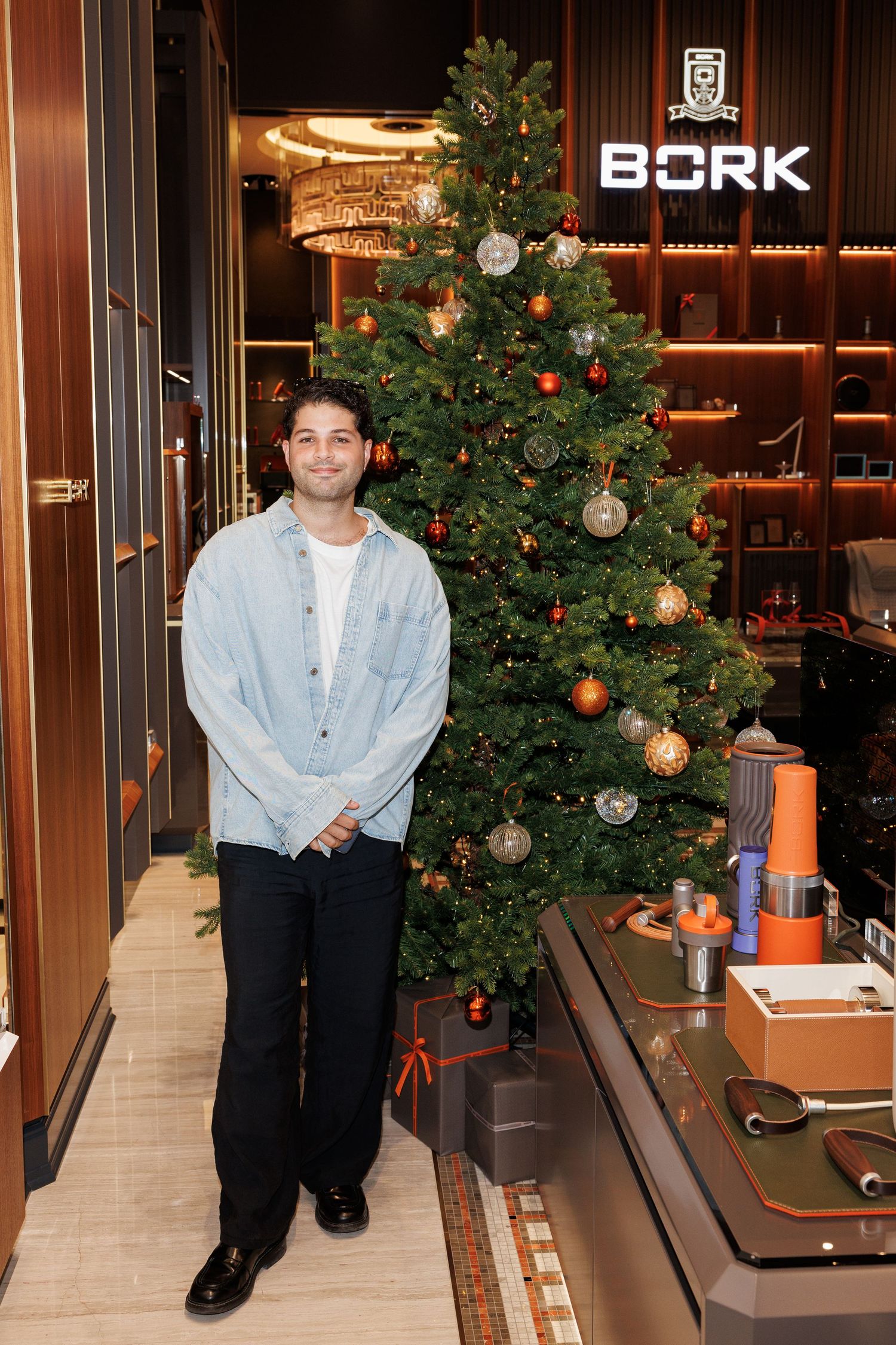 Person in light denim shirt poses near decorated Christmas tree at BORK retail store.
