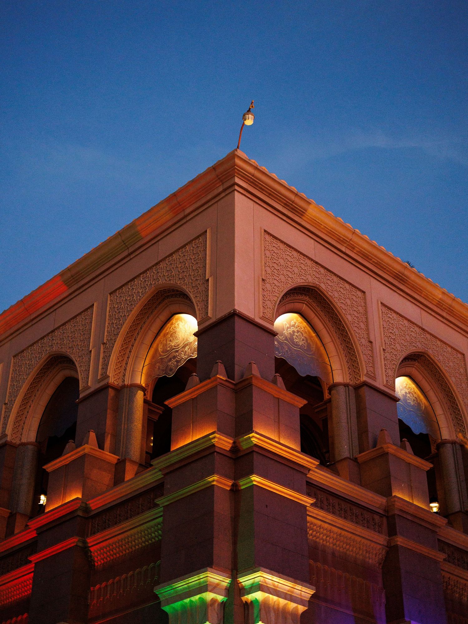 Illuminated architectural details of a Middle Eastern style building with ornate arches and terracotta colored walls at dusk.