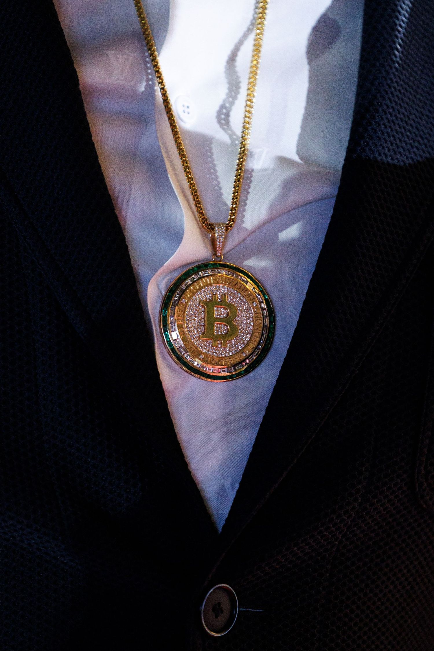 Gold Bitcoin pendant necklace on white shirt with black jacket.
