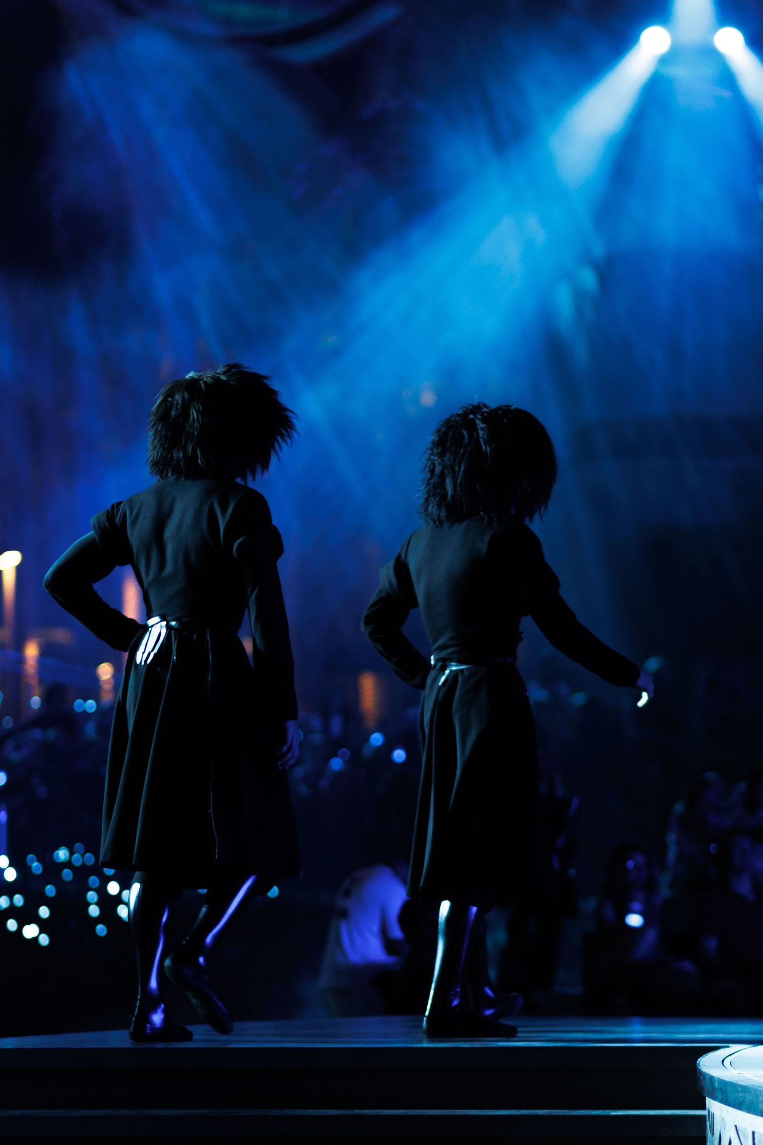 Silhouetted dancers performing against deep blue atmospheric stage lighting.