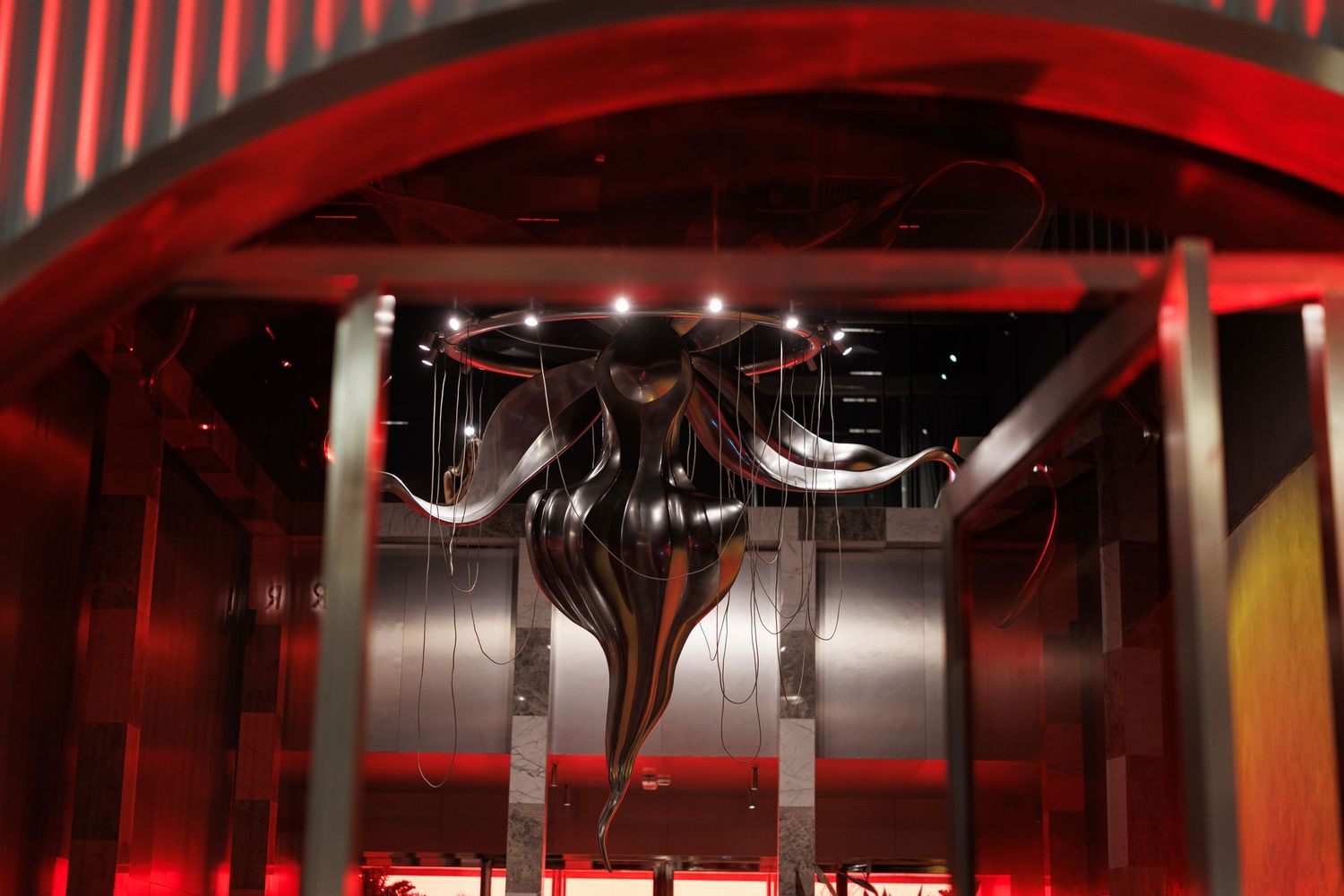 Black cables and wiring hang from a red-lit industrial ceiling structure in a dark interior space.