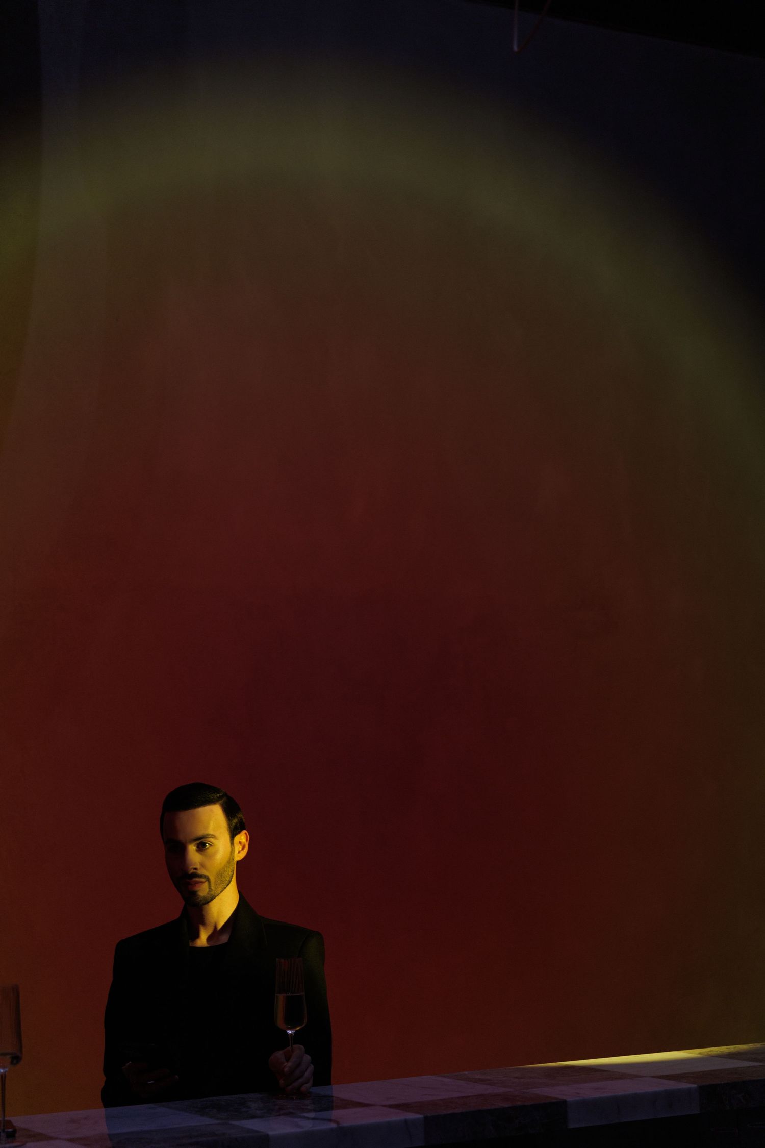 Dramatic low-key portrait with person seated at desk against dark red background.