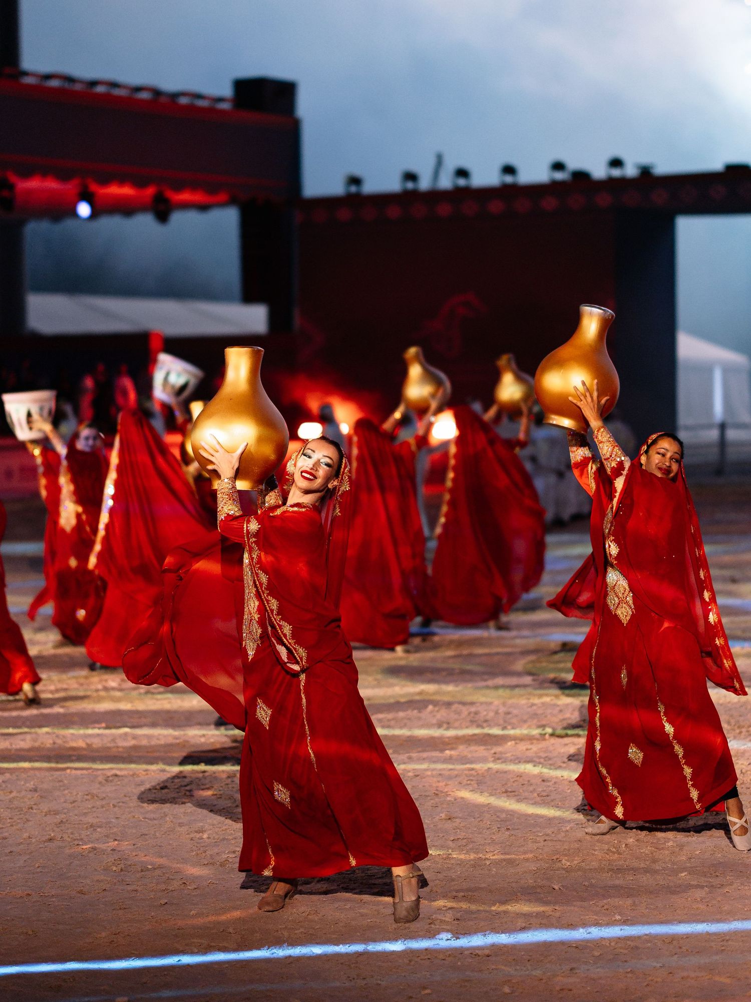 Buddhist monks in flowing red robes walk in a ceremonial procession while carrying lanterns at dusk.