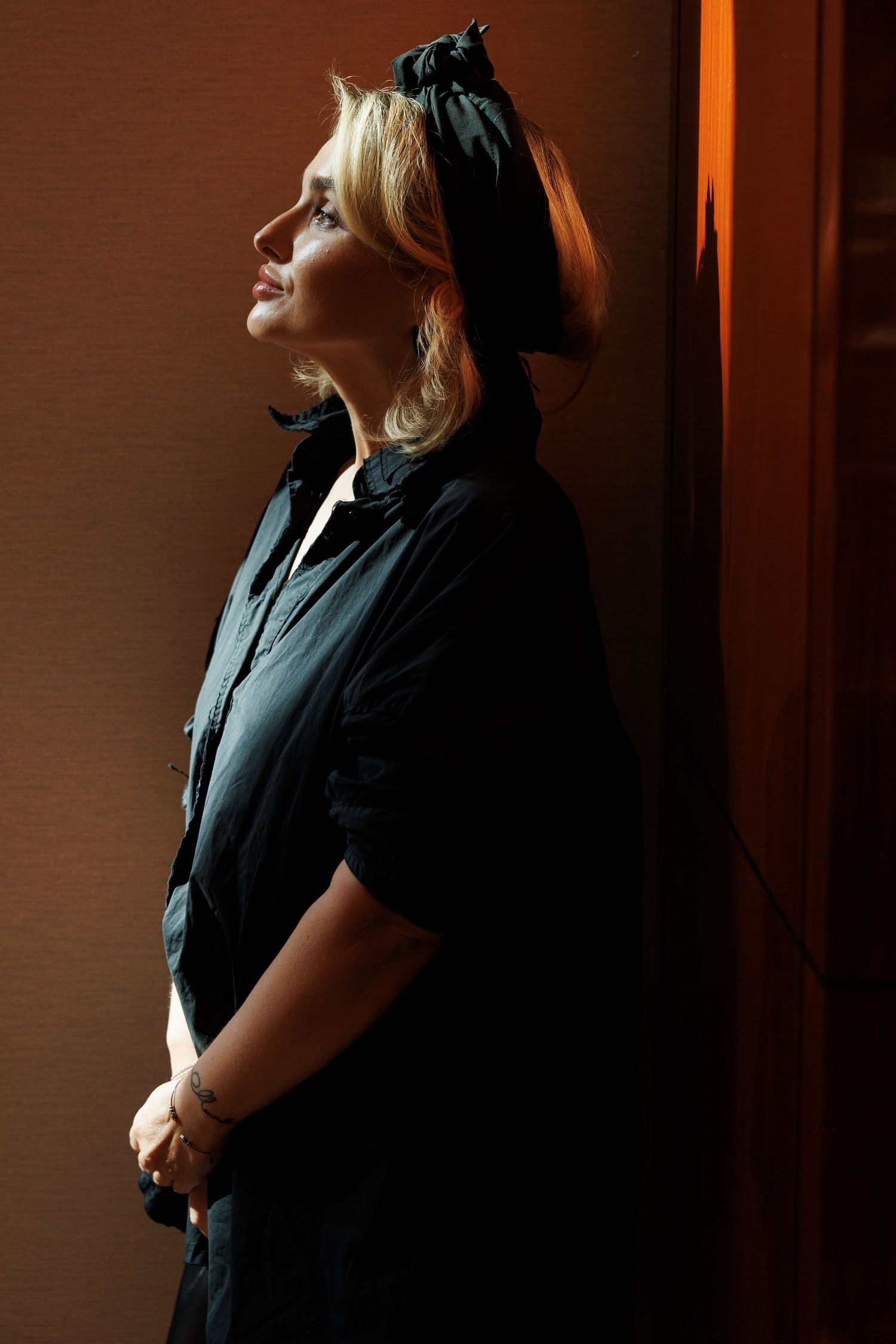 Woman in black outfit poses in front of warm-toned wall in professional photoshoot sequence.