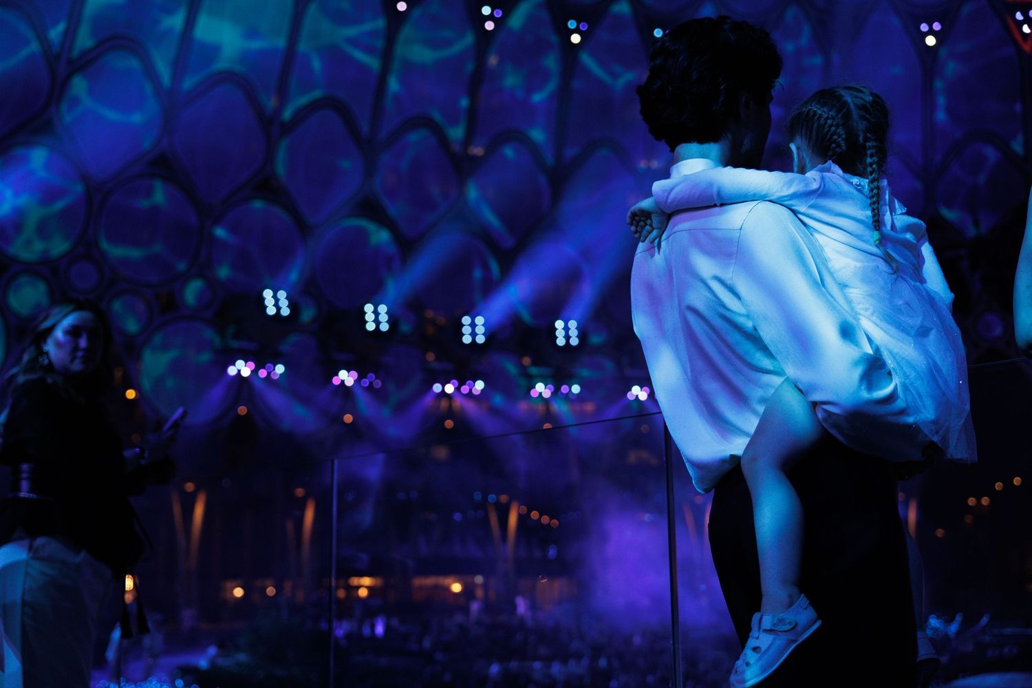 Blue-tinted concert venue with geometric ceiling patterns and crowd silhouettes.