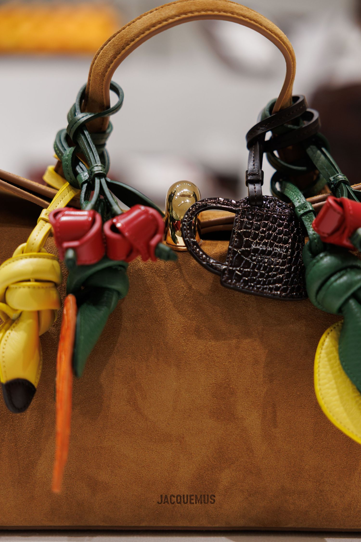 Brown leather handbag adorned with vibrant yellow, red, and green decorative charms.