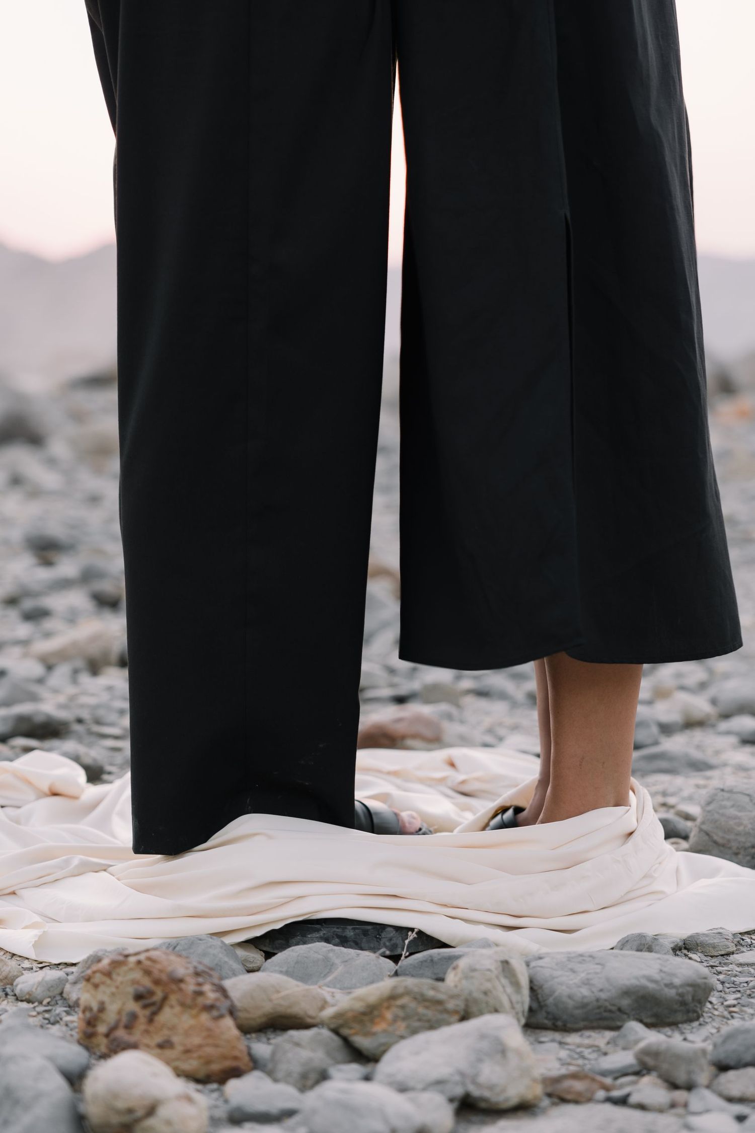 Black pants and flowing white fabric against rocky desert ground creating artistic contrast.