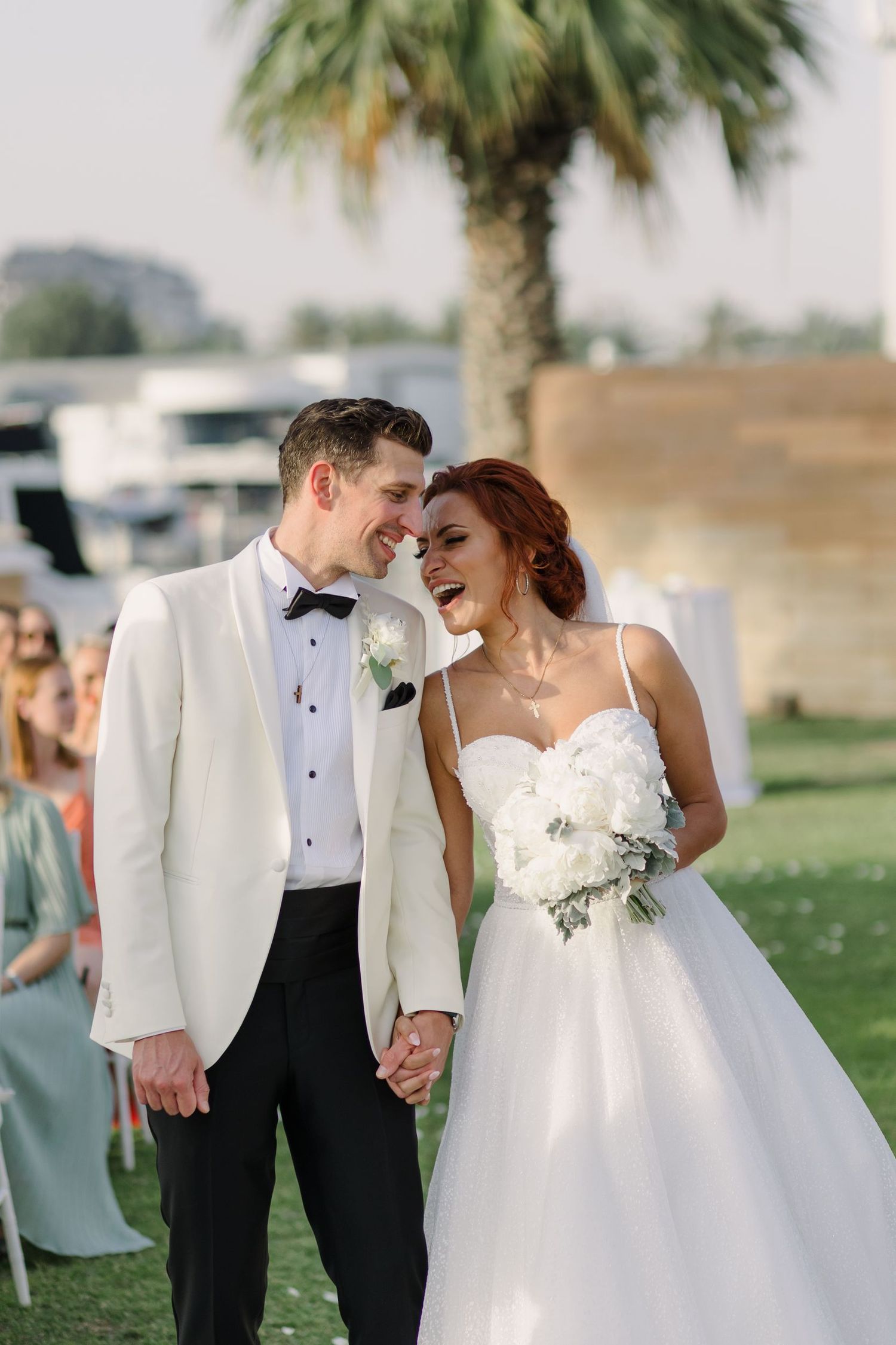 A couple in wedding attire sharing intimate moments on a lawn with palm trees.