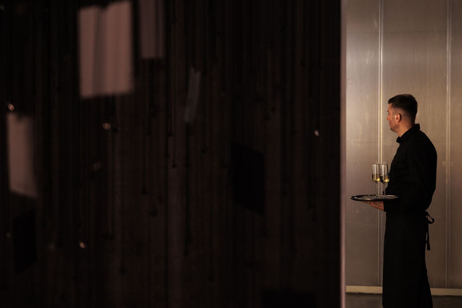 A silhouetted server holds a tray in a dimly lit hallway.