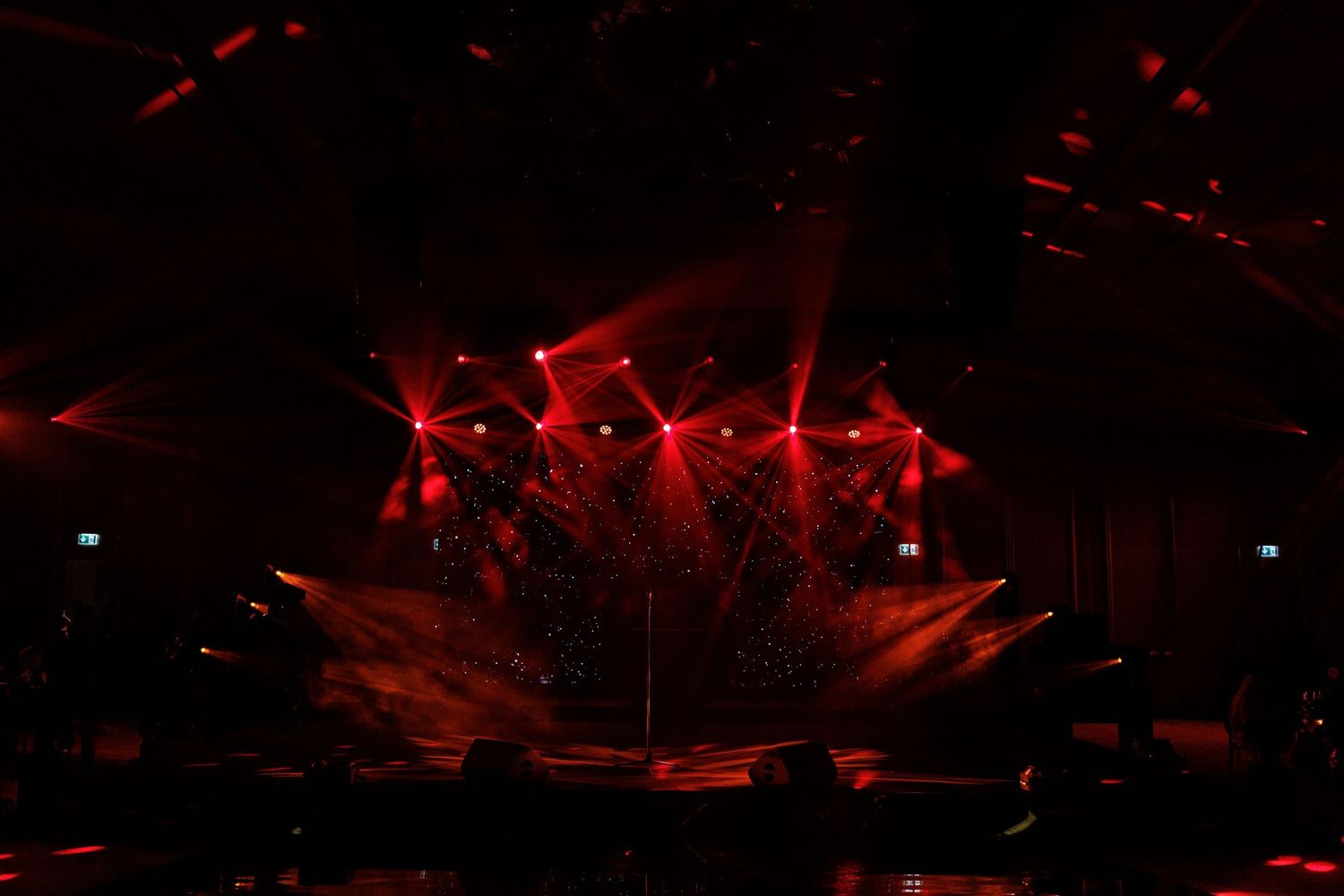 Red stage lighting creates dramatic beams and patterns across a dark performance space.