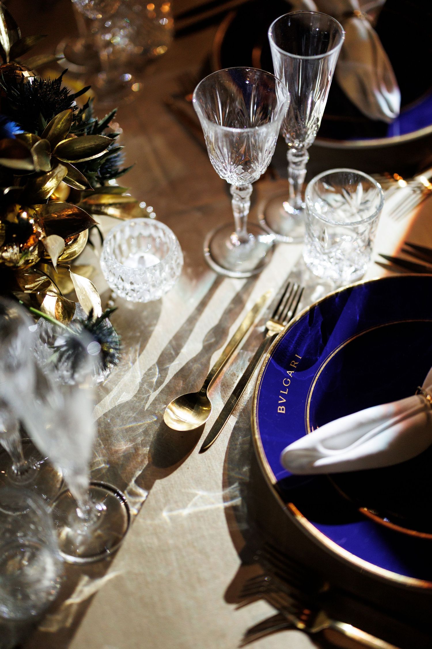 Elegant table setting with cobalt blue plates, crystal glassware, and soft lighting creating a romantic dining atmosphere.