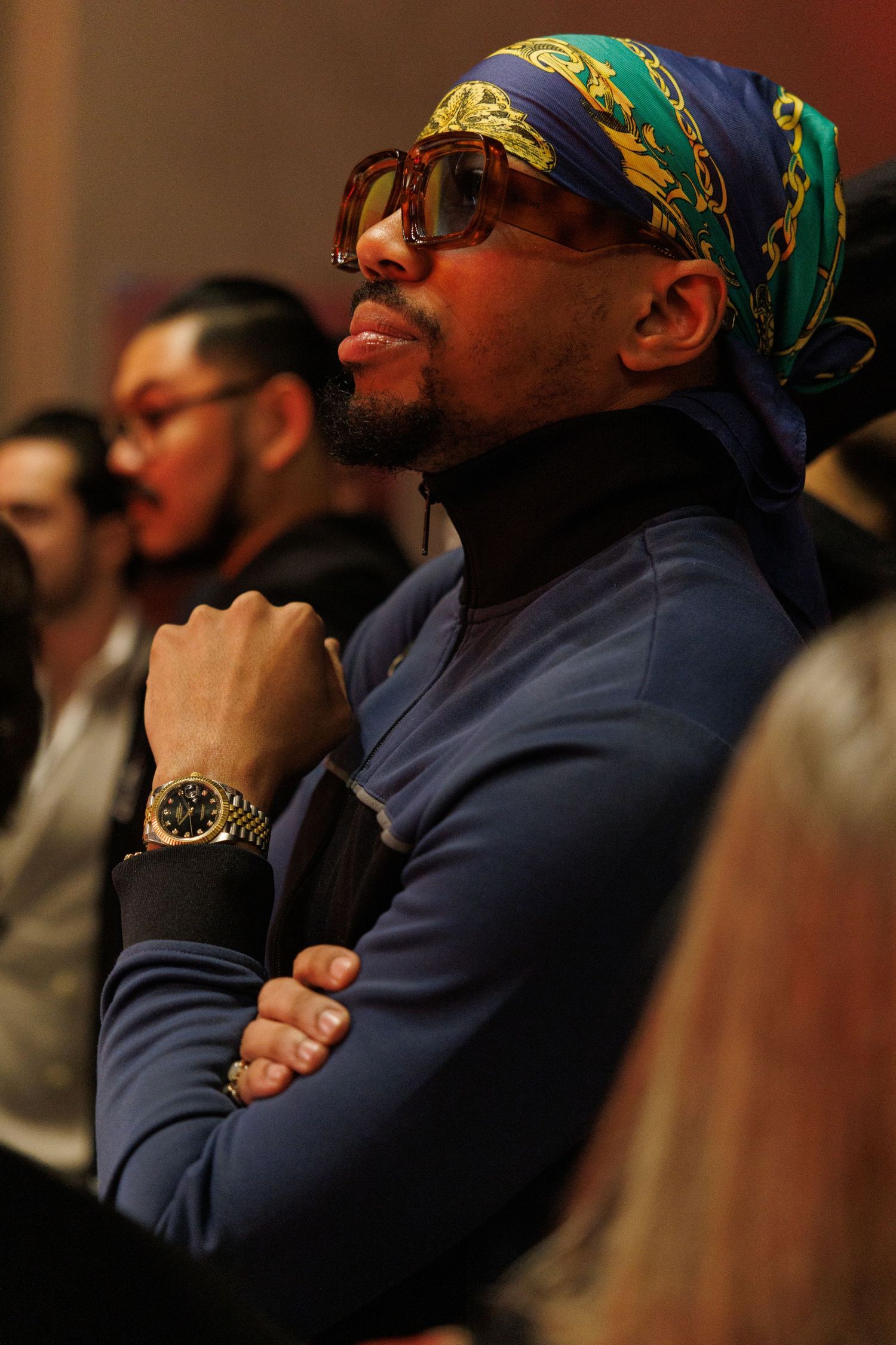 Row of audience members wearing bandanas and glasses watching intently in a darkened theater.