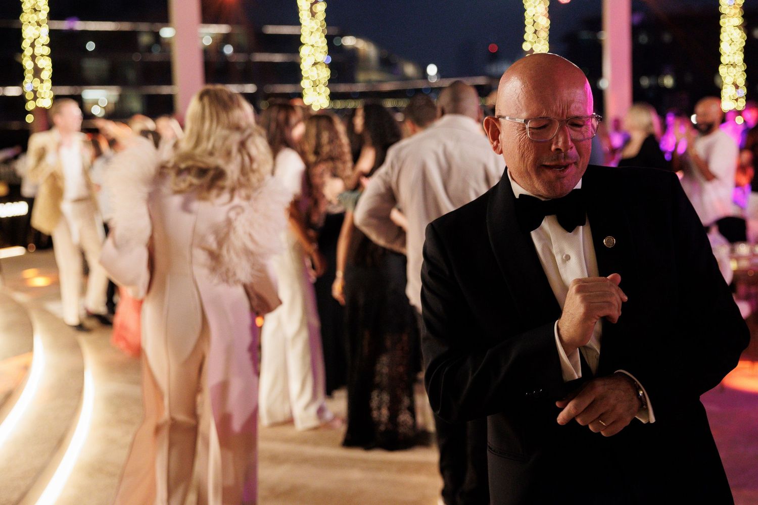 Formal event with guests in black tie attire mingling on illuminated dance floor.