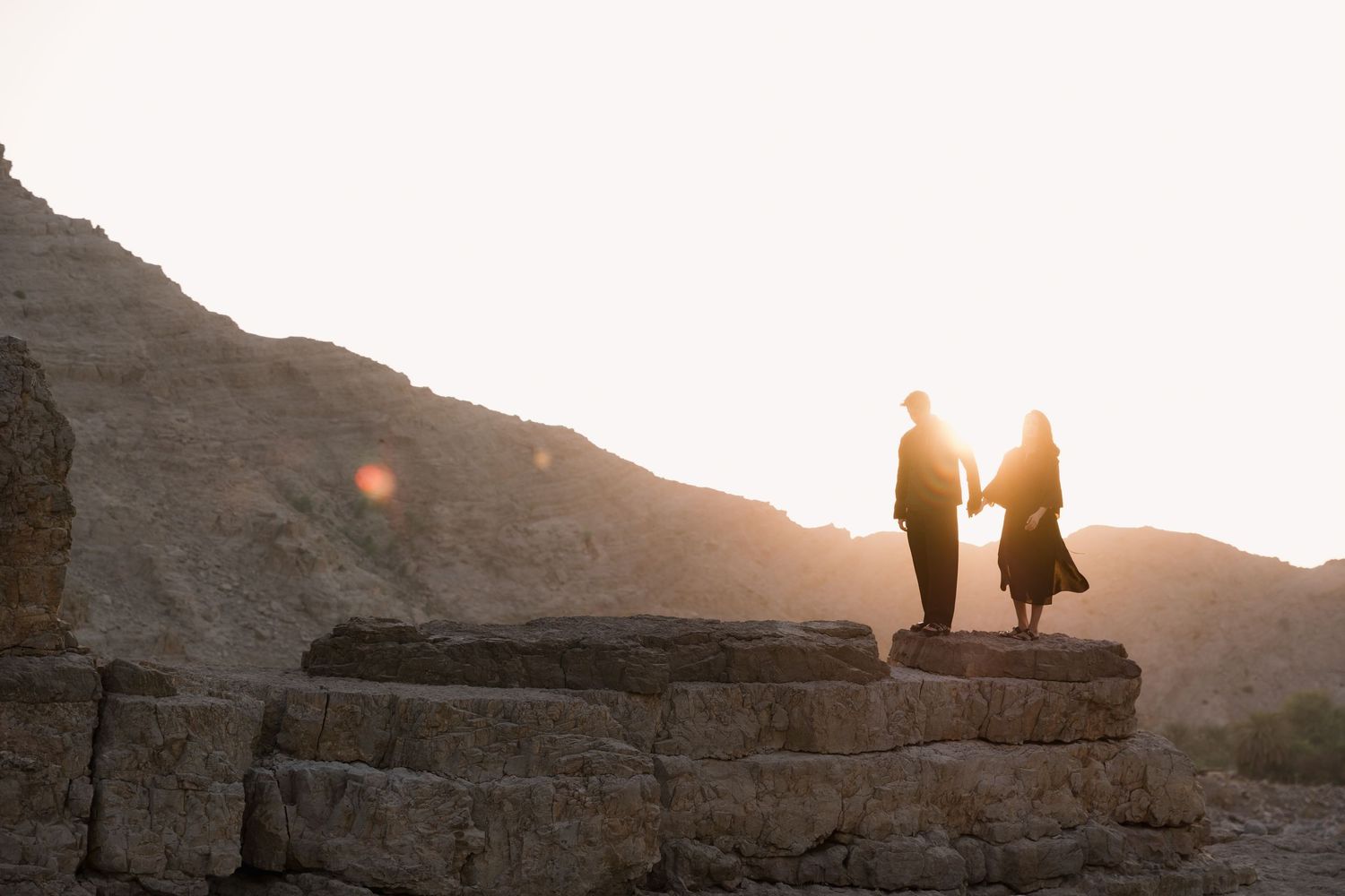 Two silhouettes standing together on a rocky cliff during golden hour.