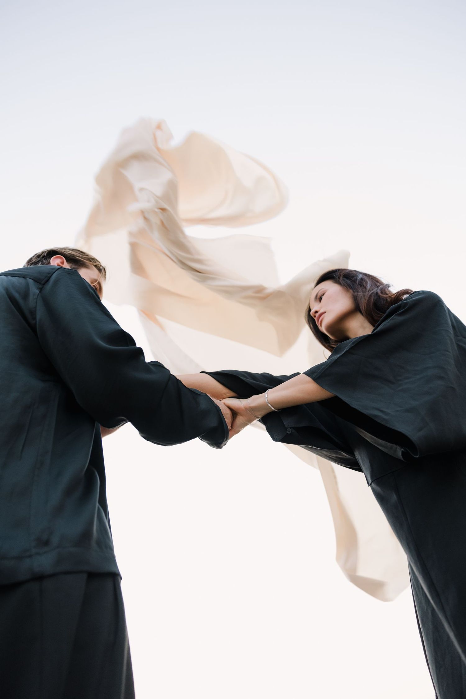 Artistic dance movement with black clothing and flowing beige fabric against white background.