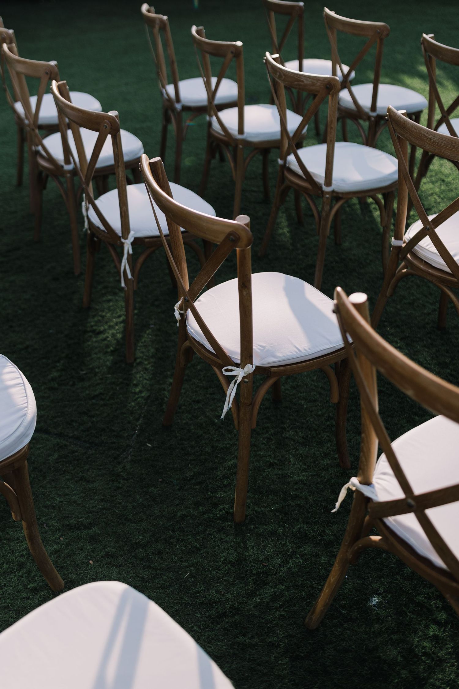 Wooden cross-back chairs arranged on grass for outdoor wedding ceremony.