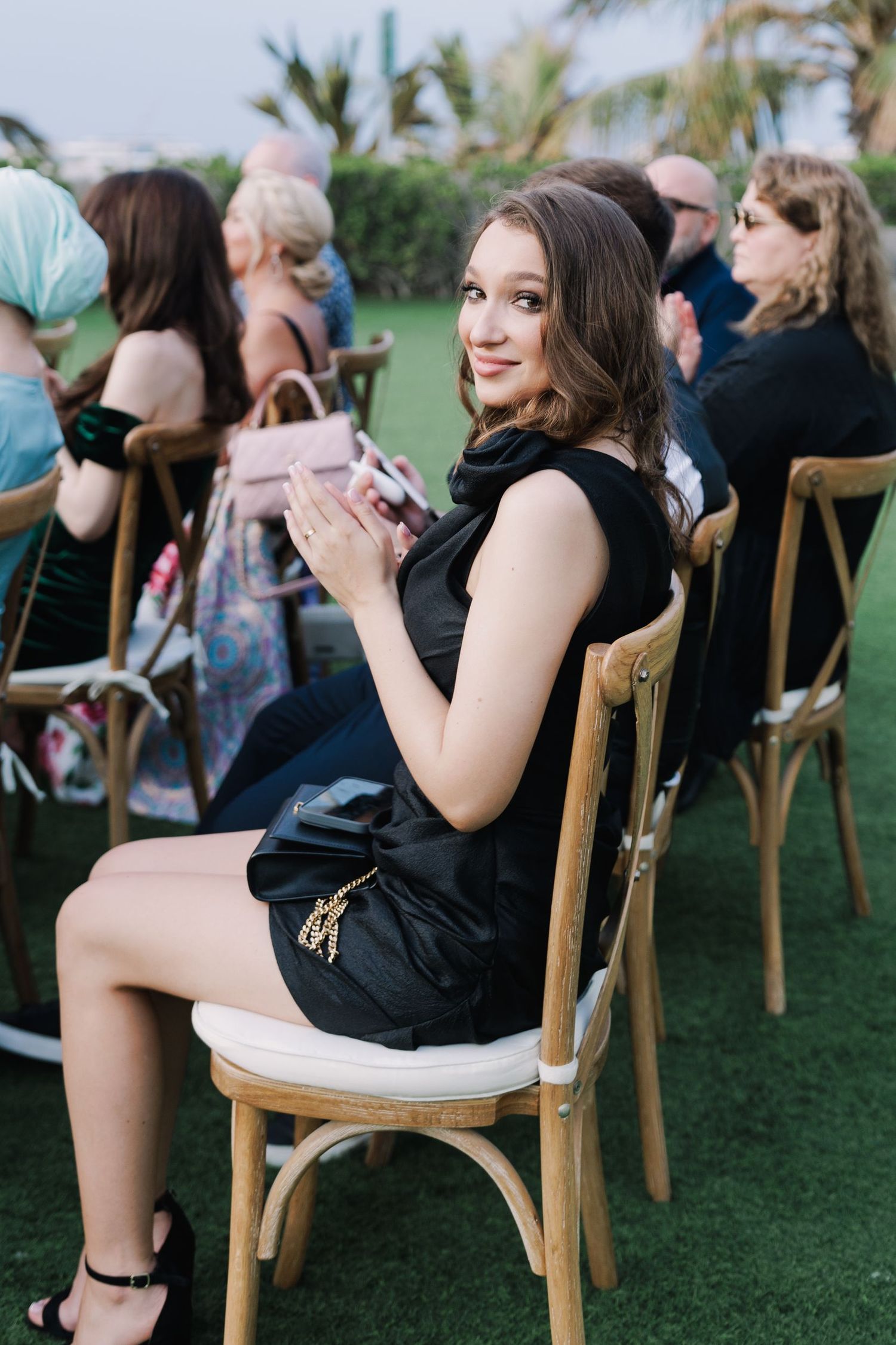 Guests seated in wooden cross-back chairs during an outdoor celebration.