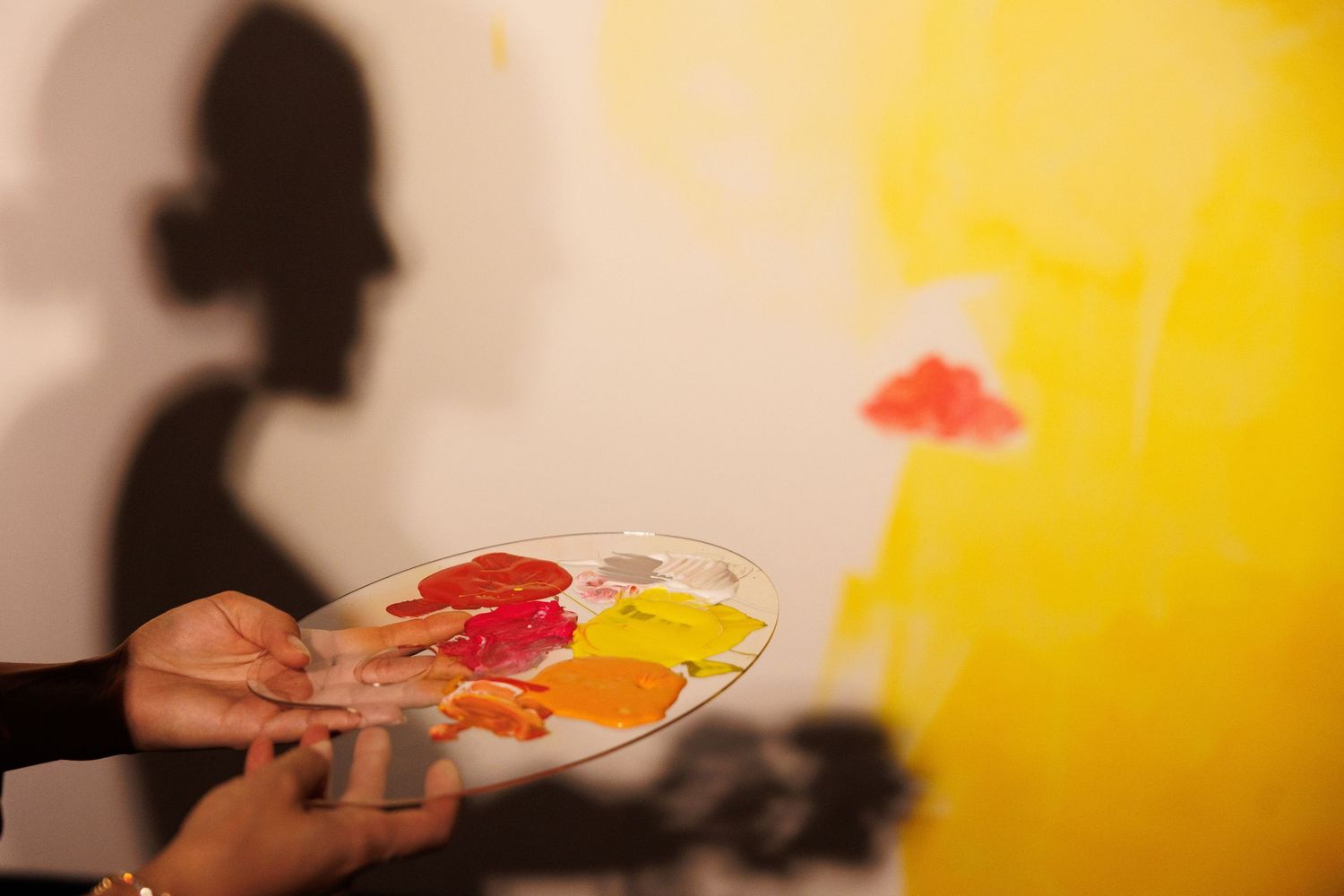 Artist holding a paint palette with vibrant colors against a yellow wall.