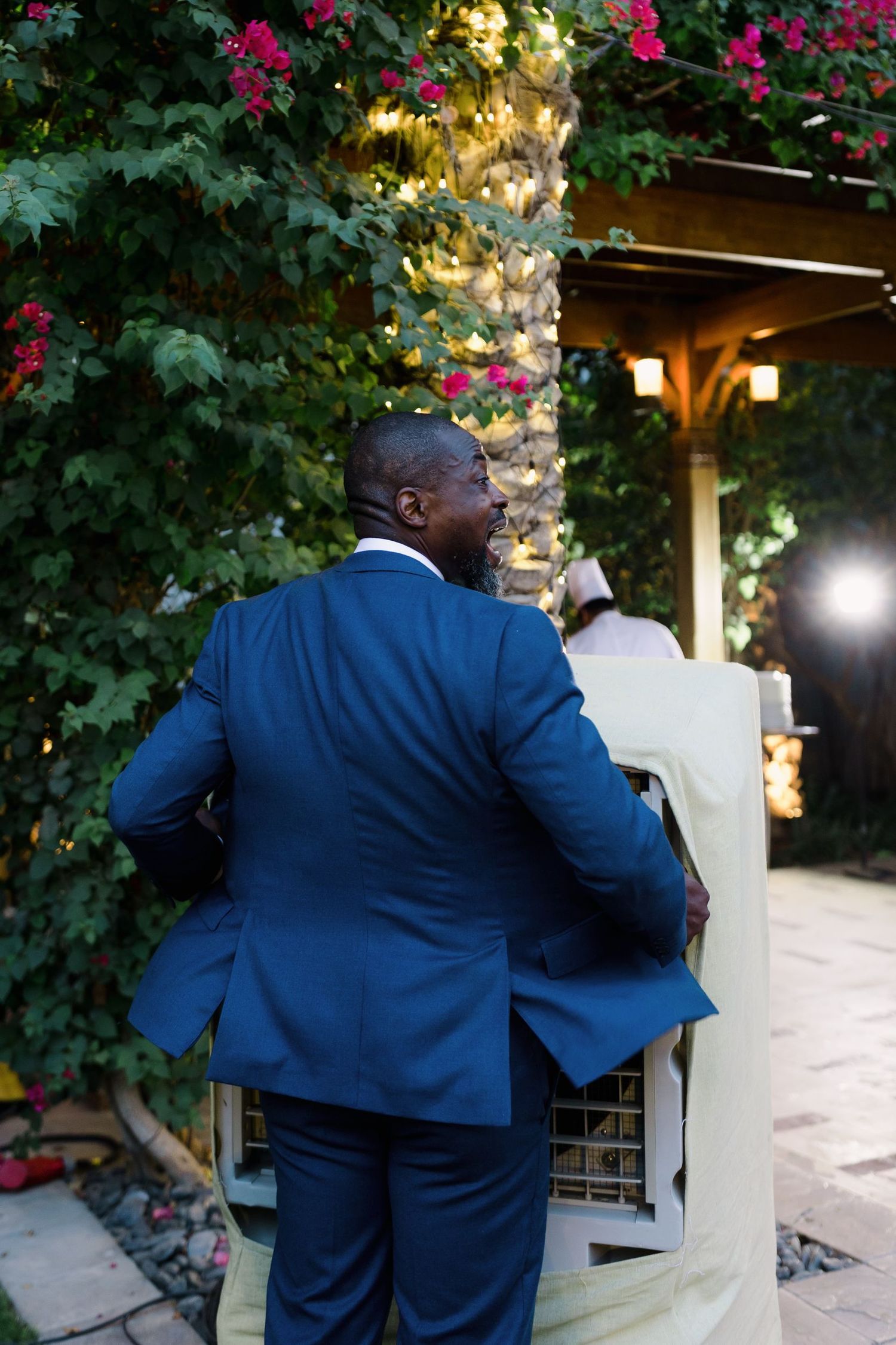 Guest in blue suit standing near illuminated floral arrangements at evening wedding reception.