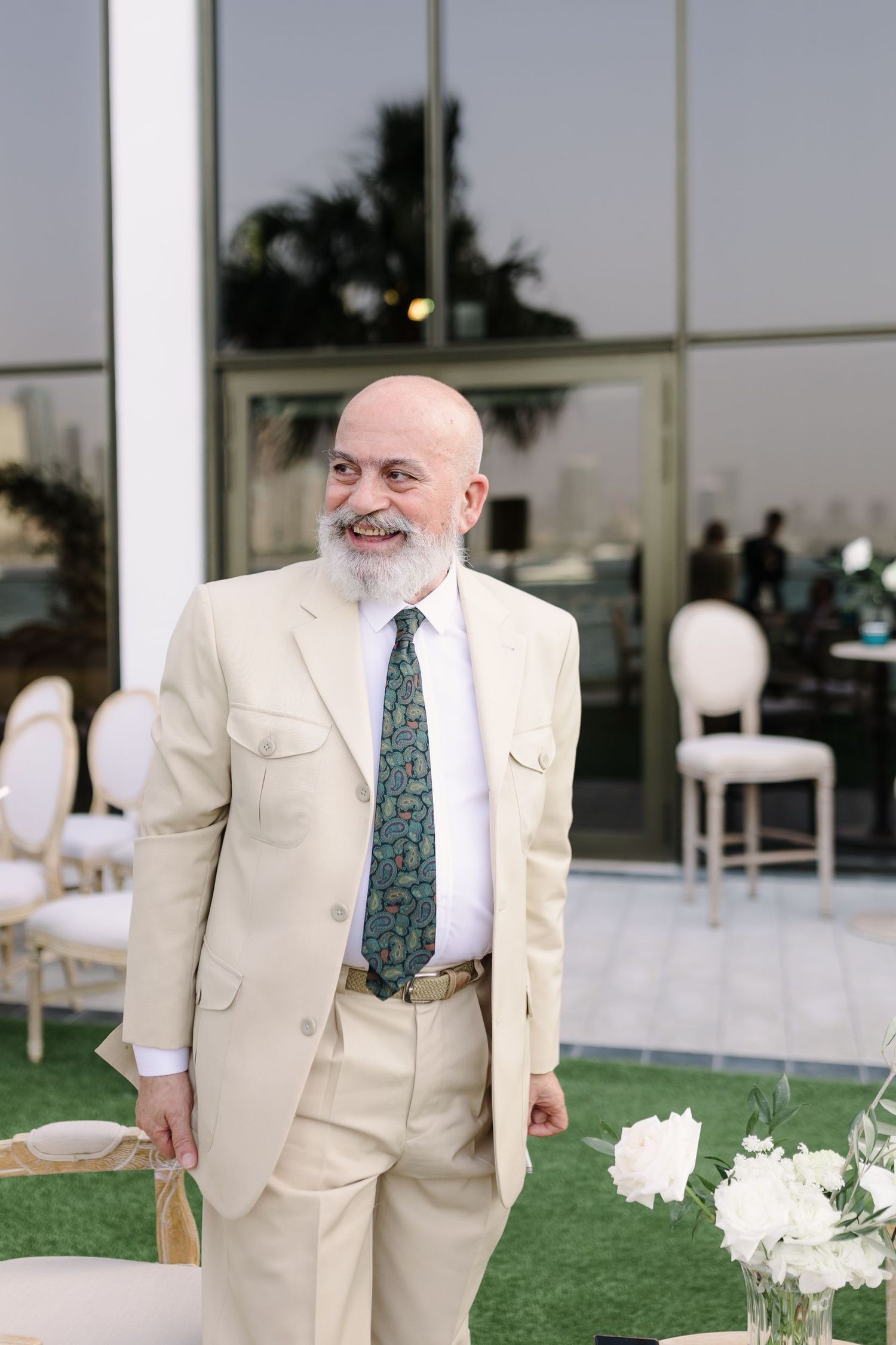 Wedding guest in a cream colored suit walks through an outdoor ceremony space.
