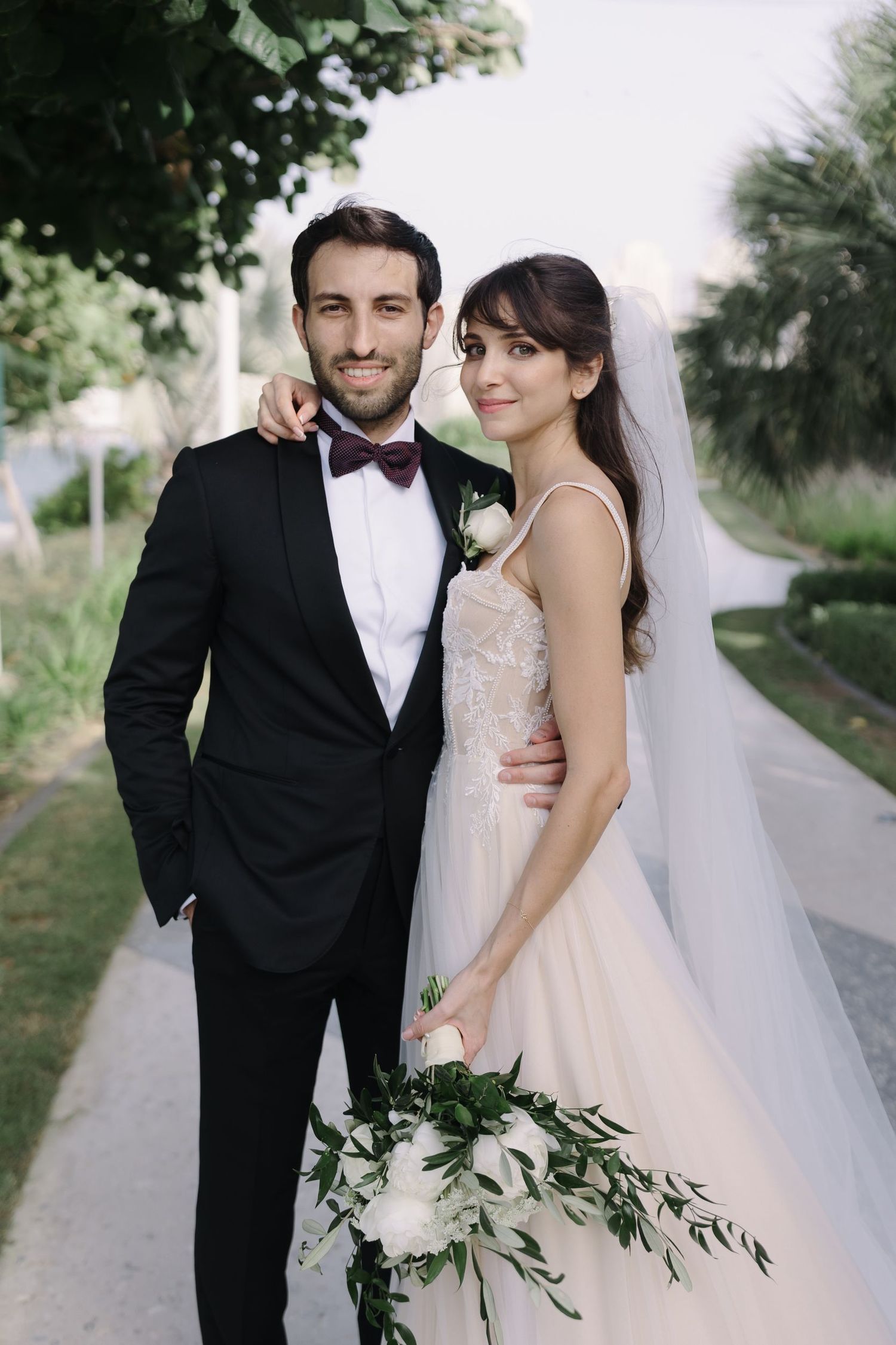 Elegant bride and groom posing together on a garden path with natural foliage.