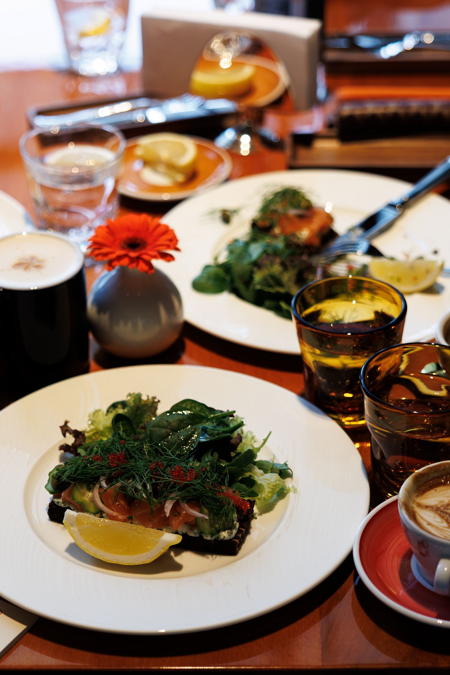 Elegant plated dishes with salads, drinks and a decorative orange flower on a restaurant table.