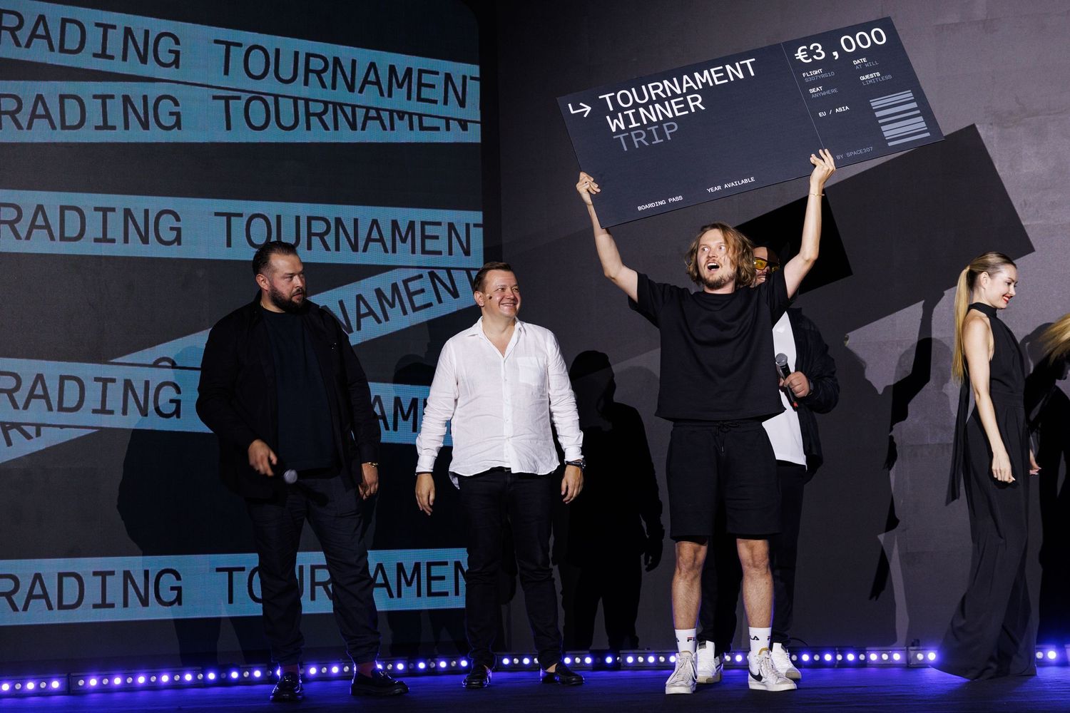 Winner celebrates on stage at trading tournament with arms raised holding prize.