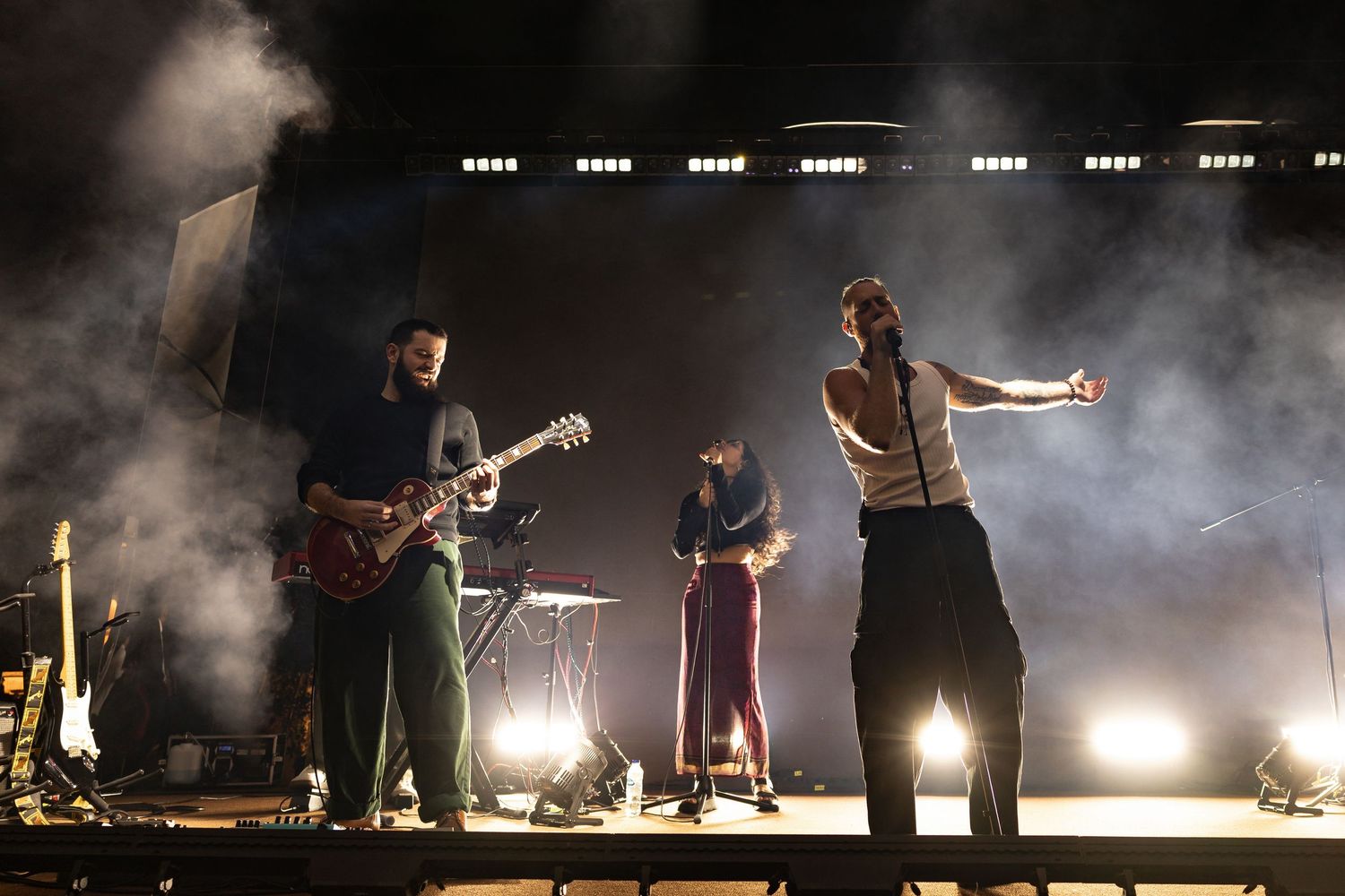 Silhouetted musicians perform on a smoky stage with dramatic backlighting creating an atmospheric concert scene.