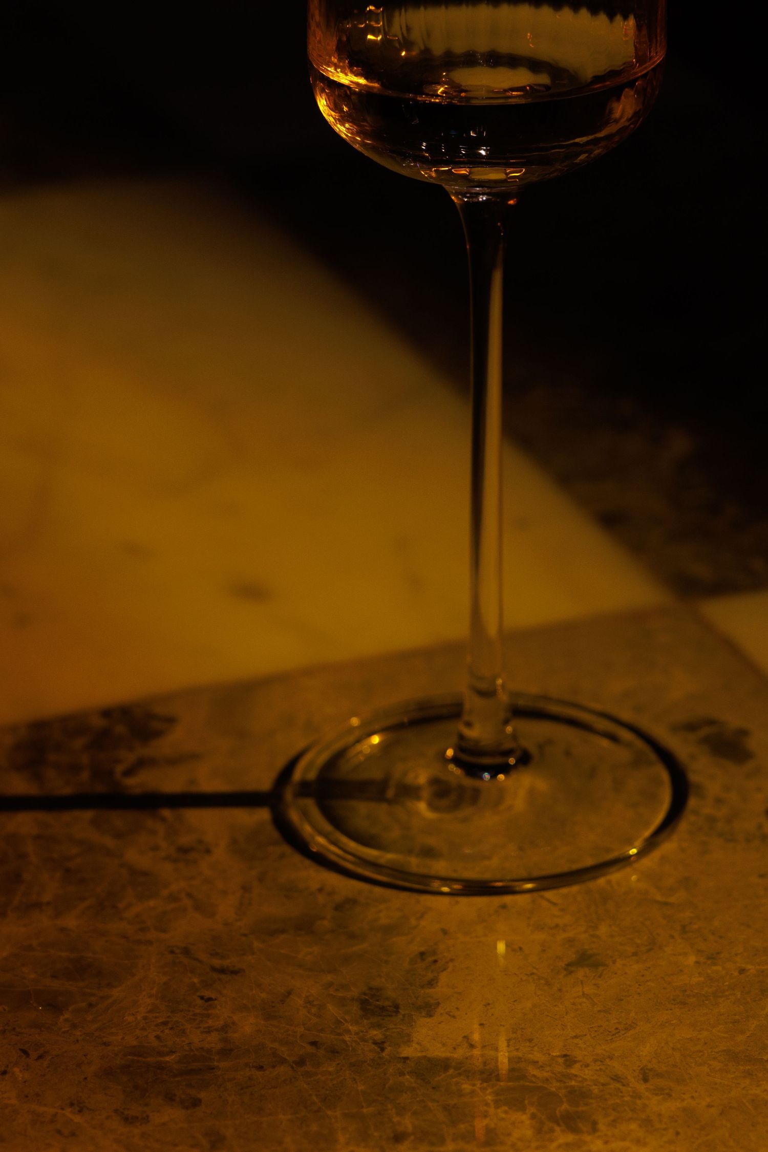Close-up of wine glass stem on textured surface with warm ambient lighting.