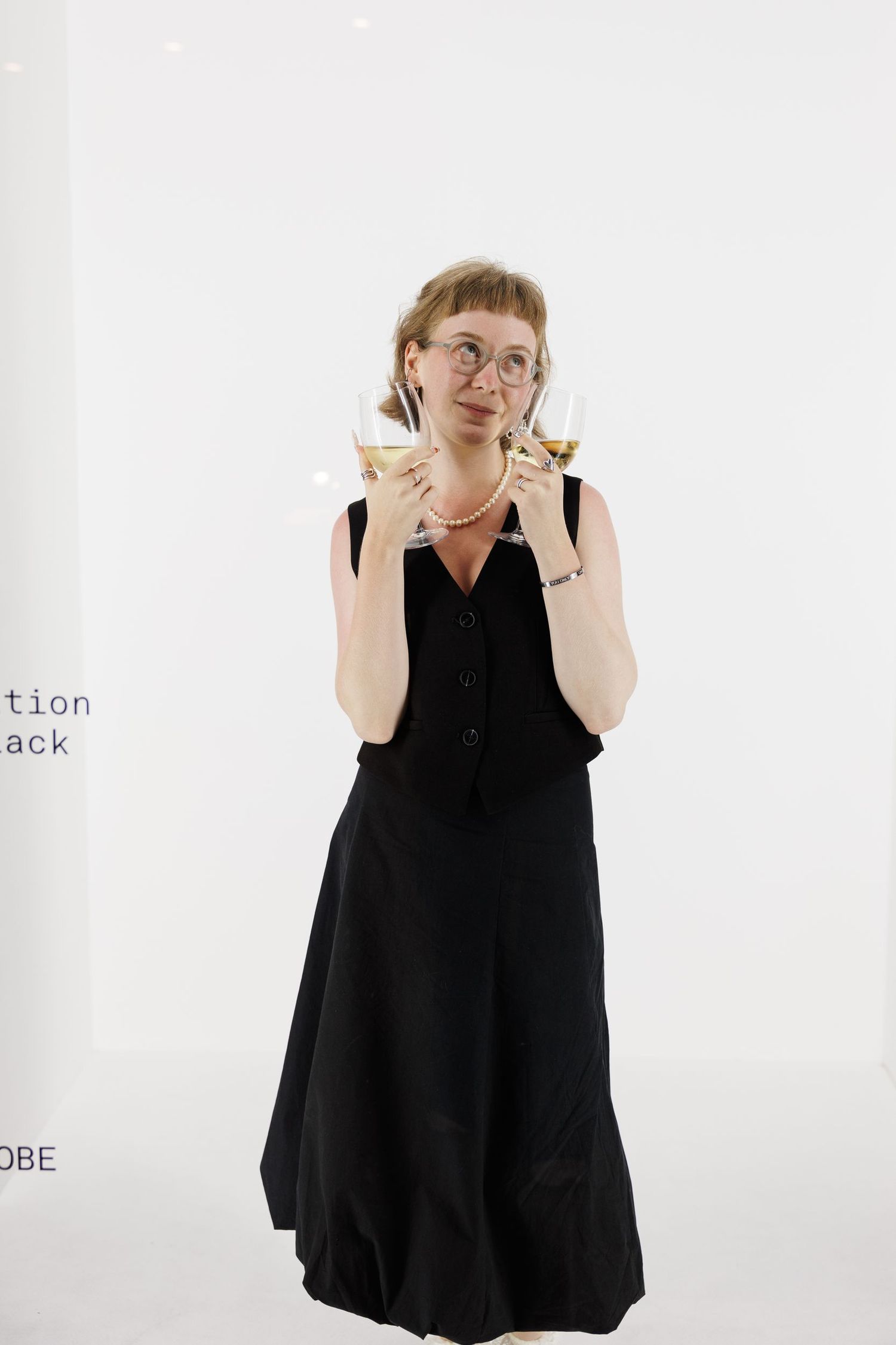 Fashion model in flowing black dress poses expressively against white background.