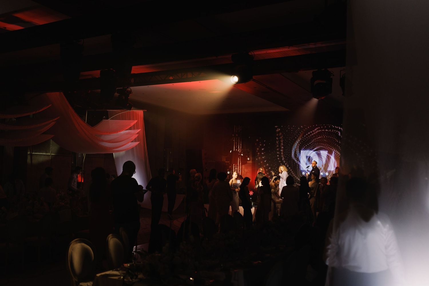 Dark event space with red ambient lighting and crowd silhouettes.