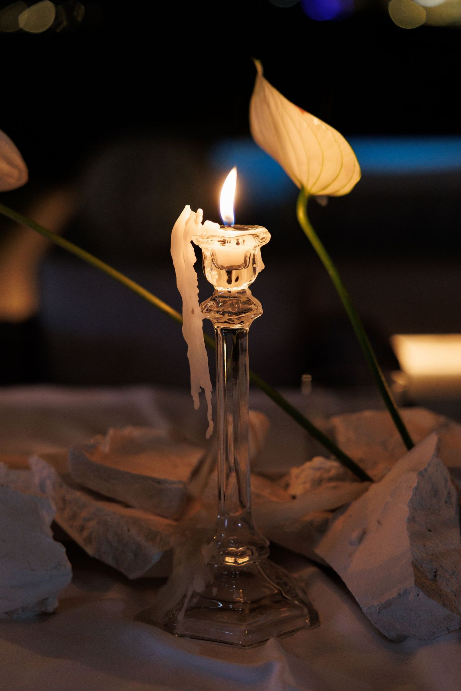 A lit candle in a glass holder with a calla lily flower against a dark background.