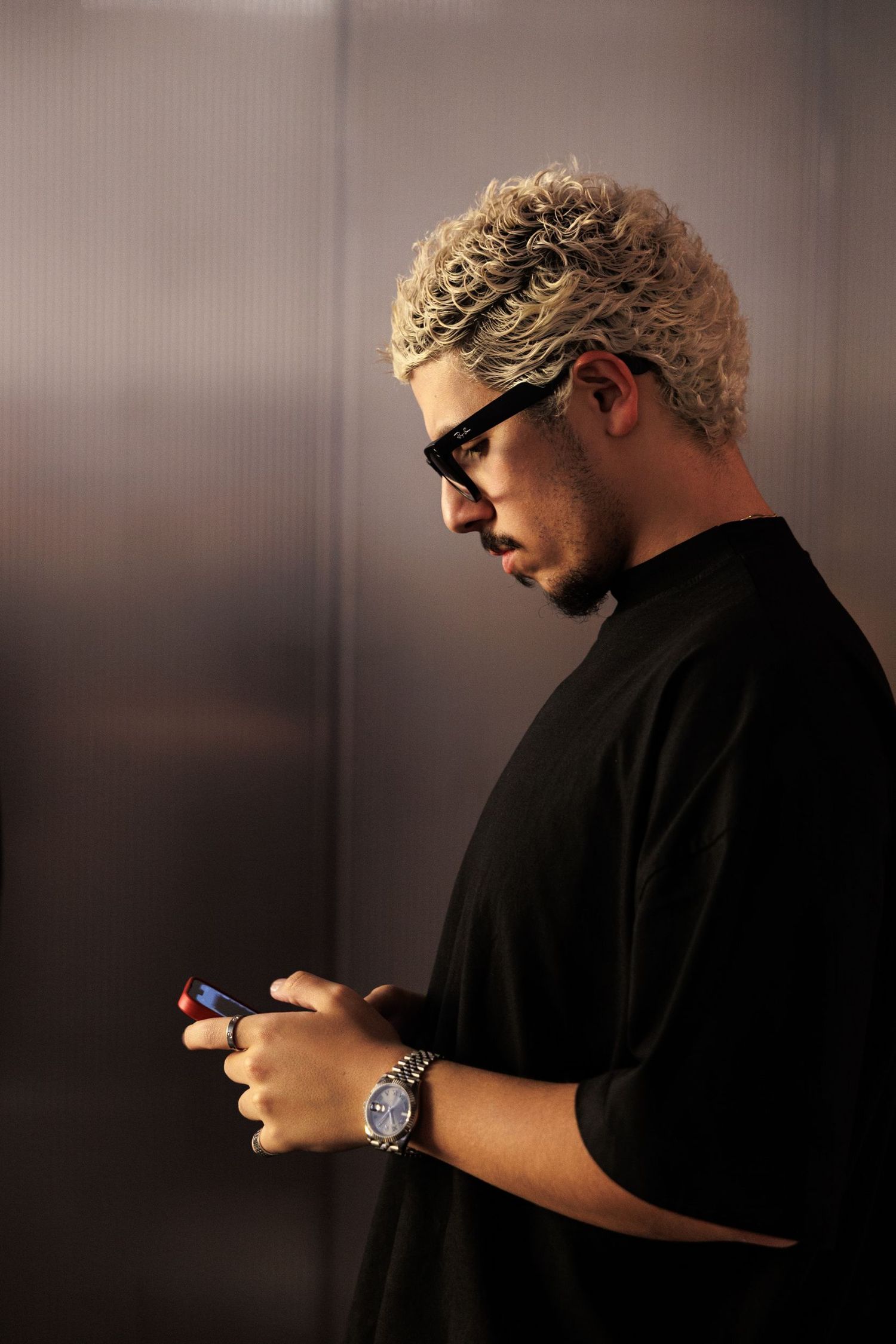 Person in black clothing using mobile phone in minimalist setting.