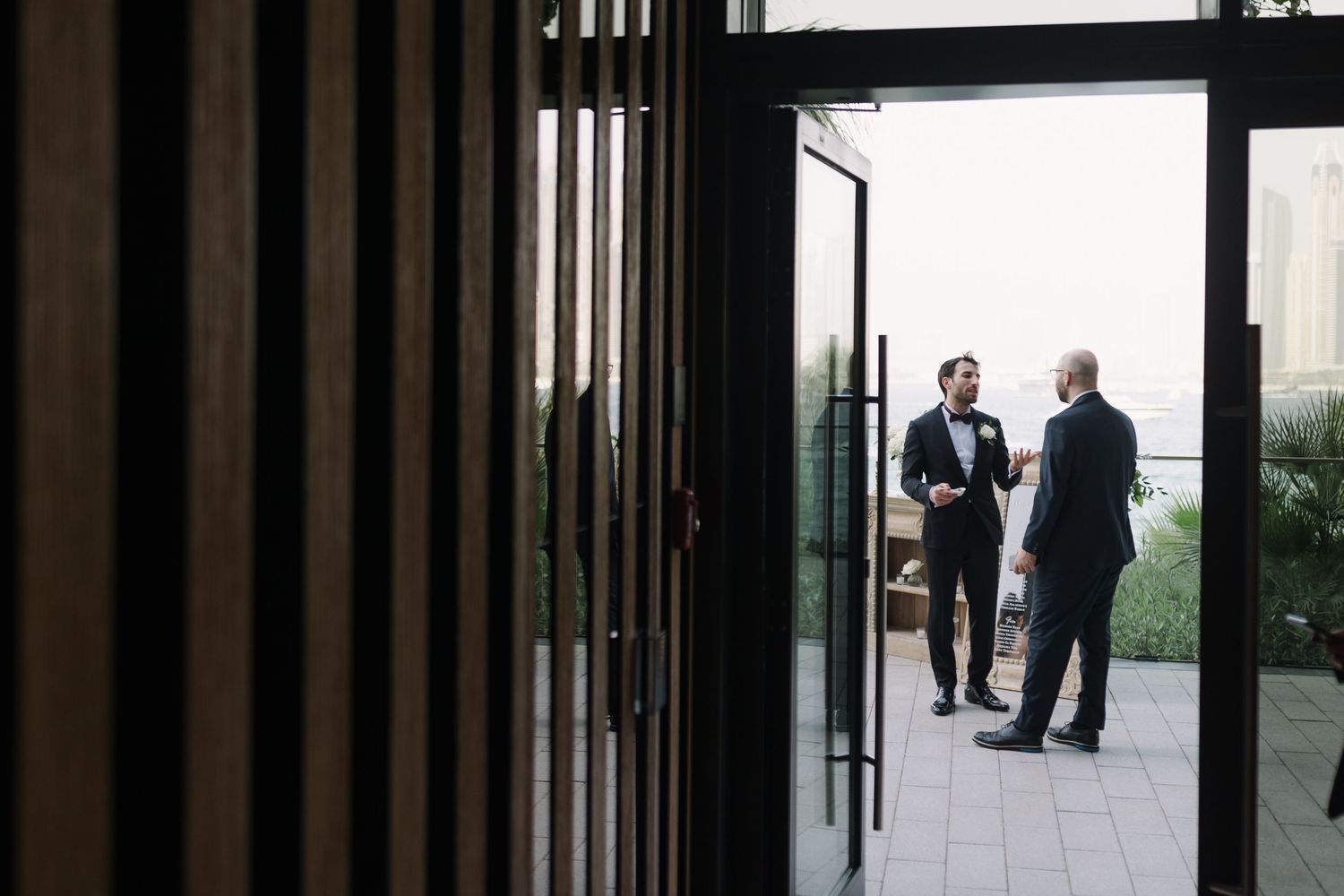 Wedding guests and venue staff seen through vertical window frames.