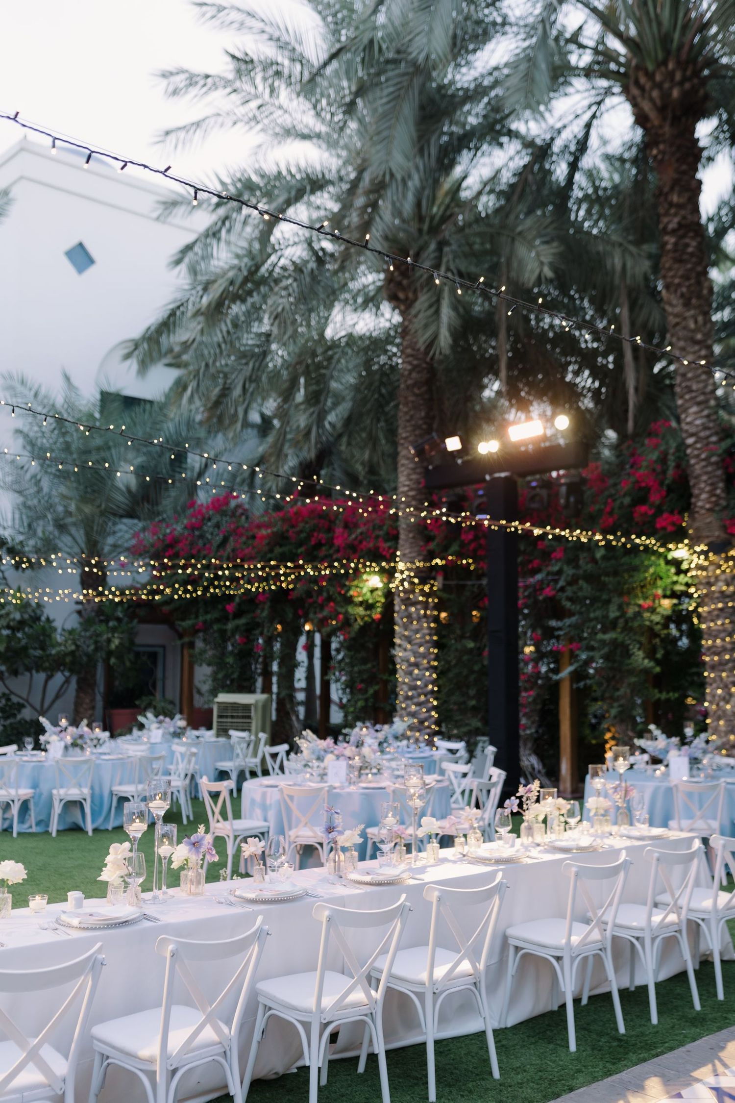 Elegant outdoor wedding reception setup with string lights and palm trees at dusk.