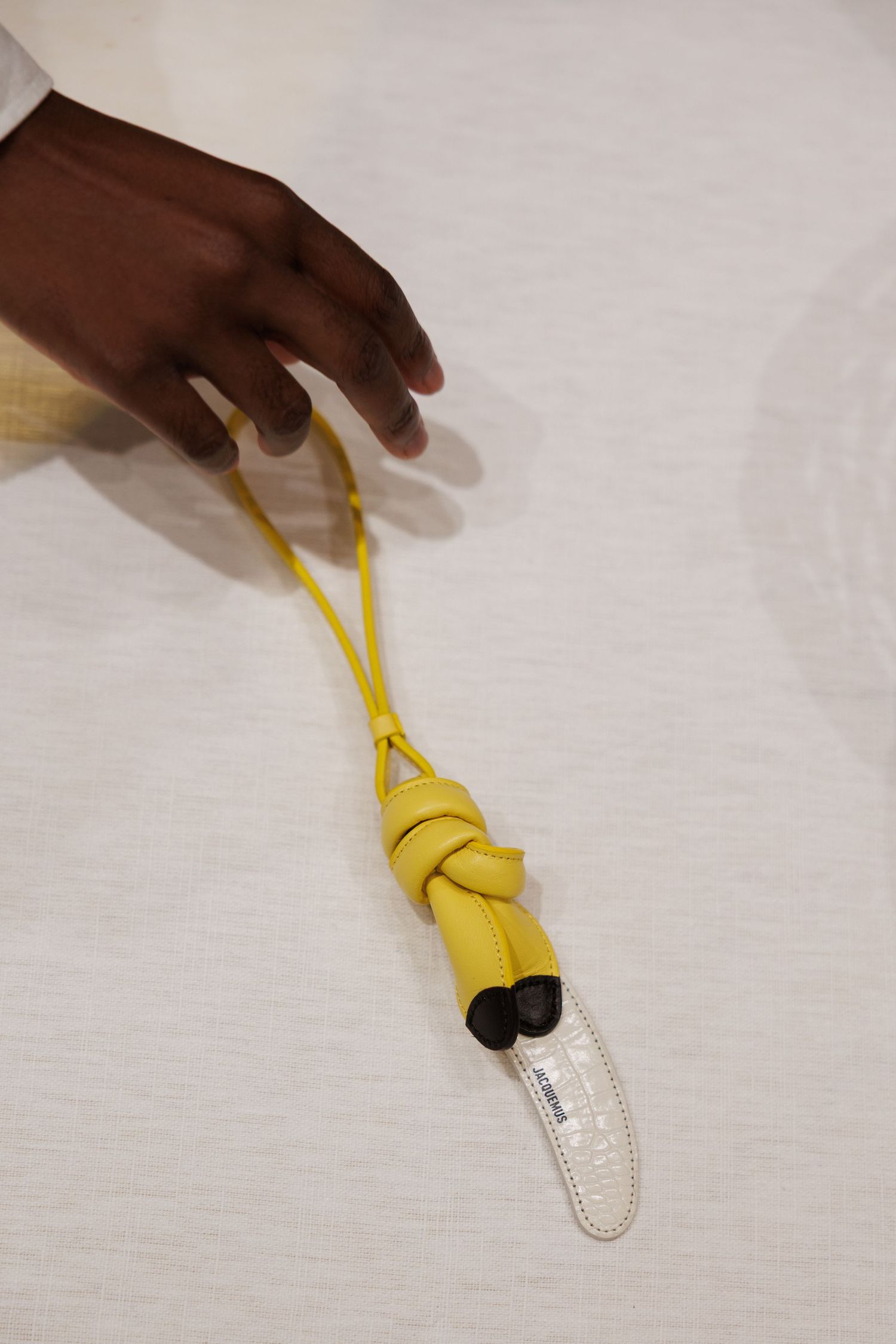 Hand holding yellow leather knotted accessory against white background.