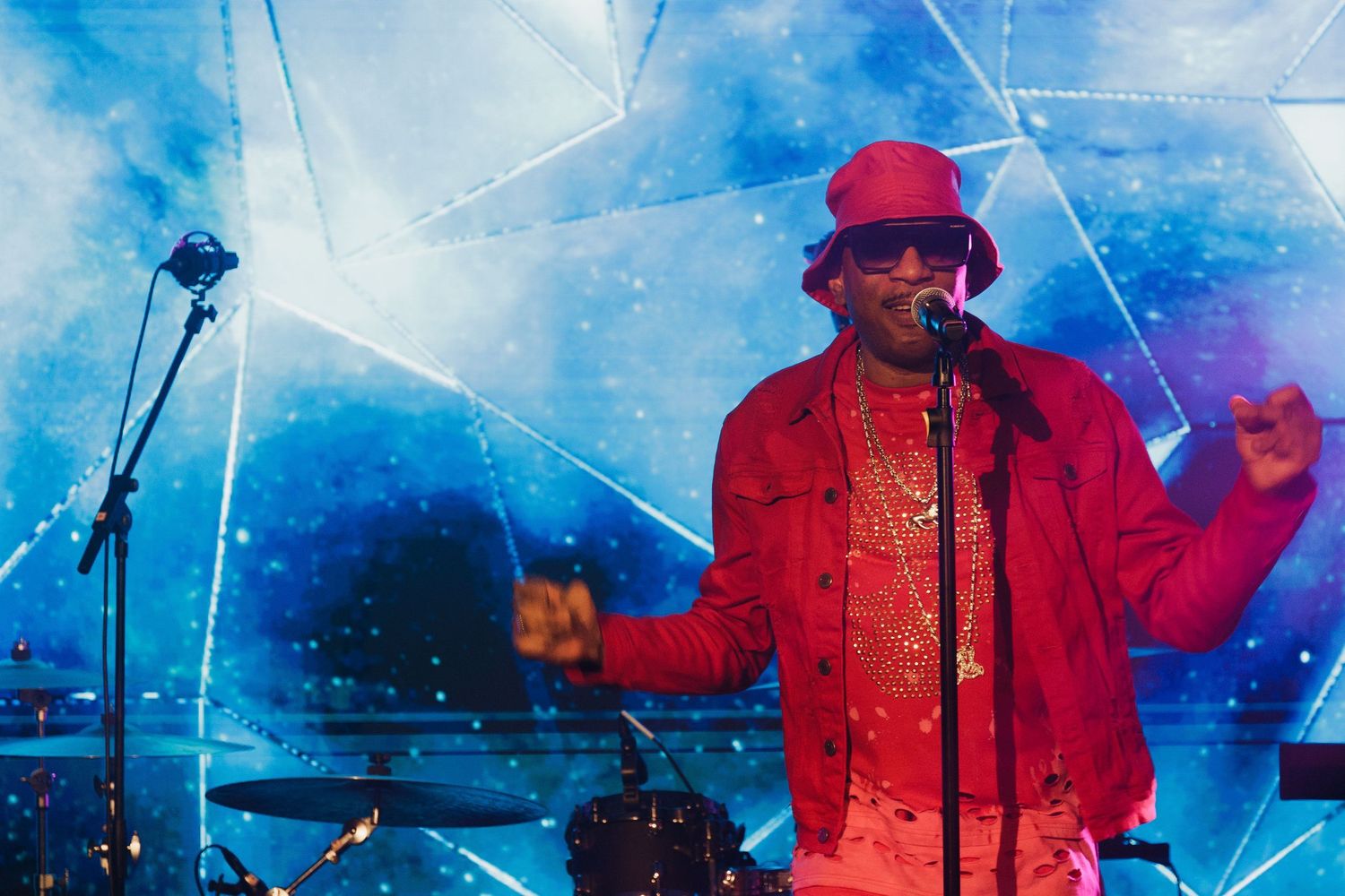 Performer in red attire on stage with dramatic blue lighting and special effects.