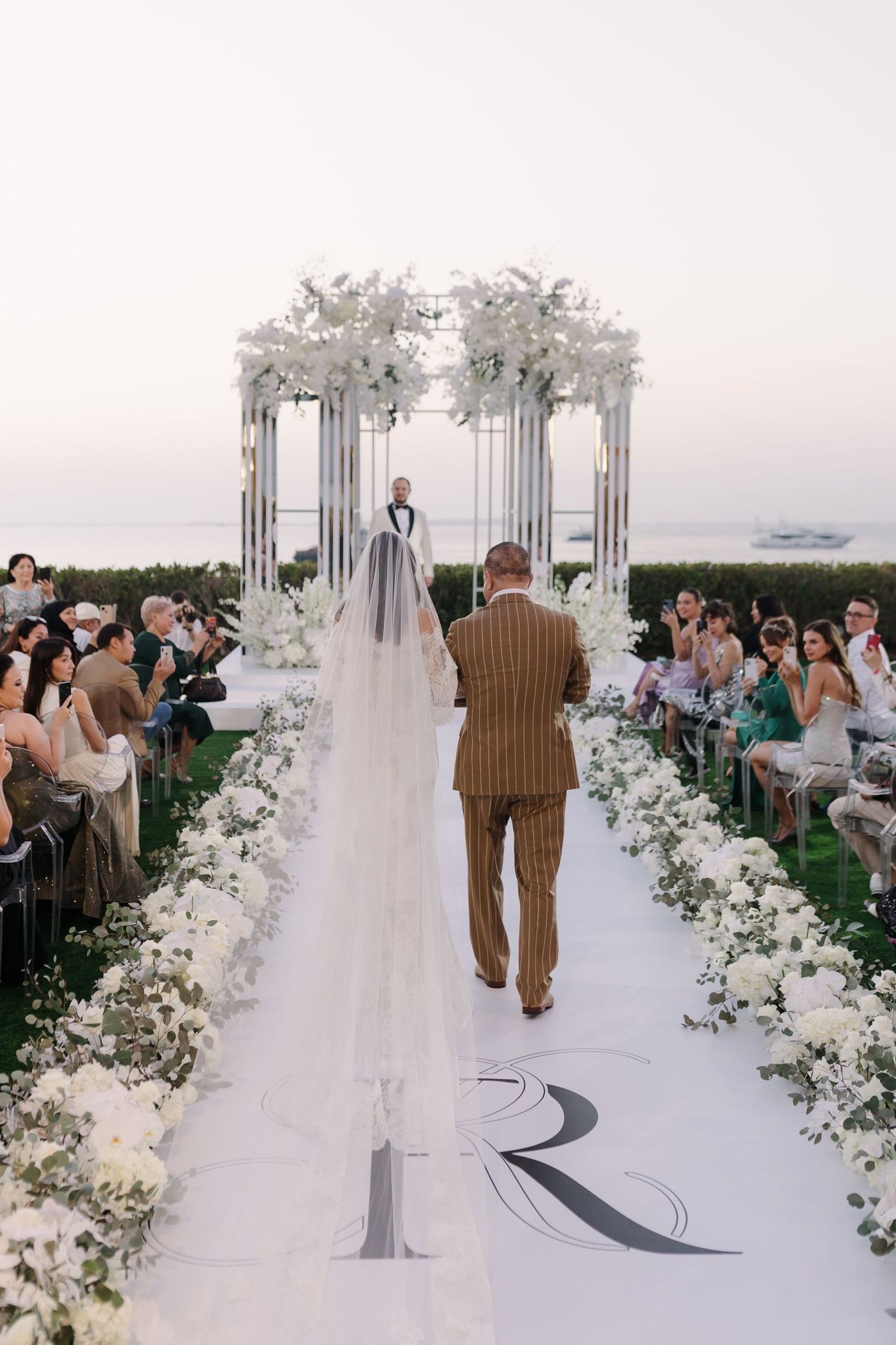 White floral arch and aisle decorations at a beachside wedding ceremony.