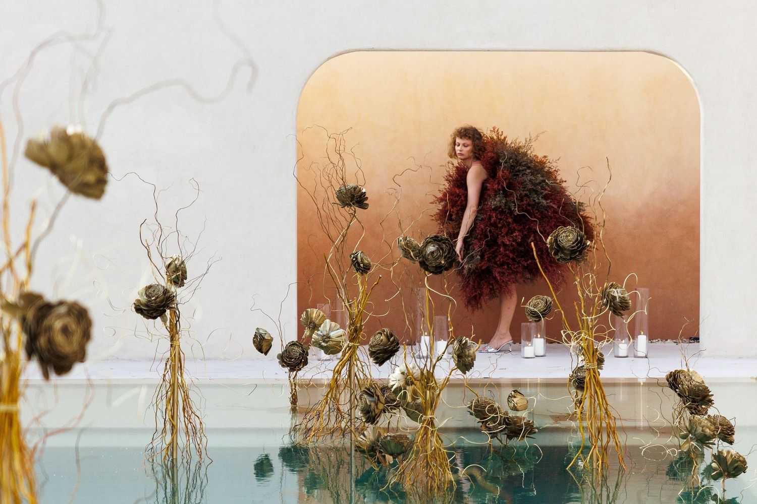 Artistic photo with dried flowers and figure reflected in water surface.
